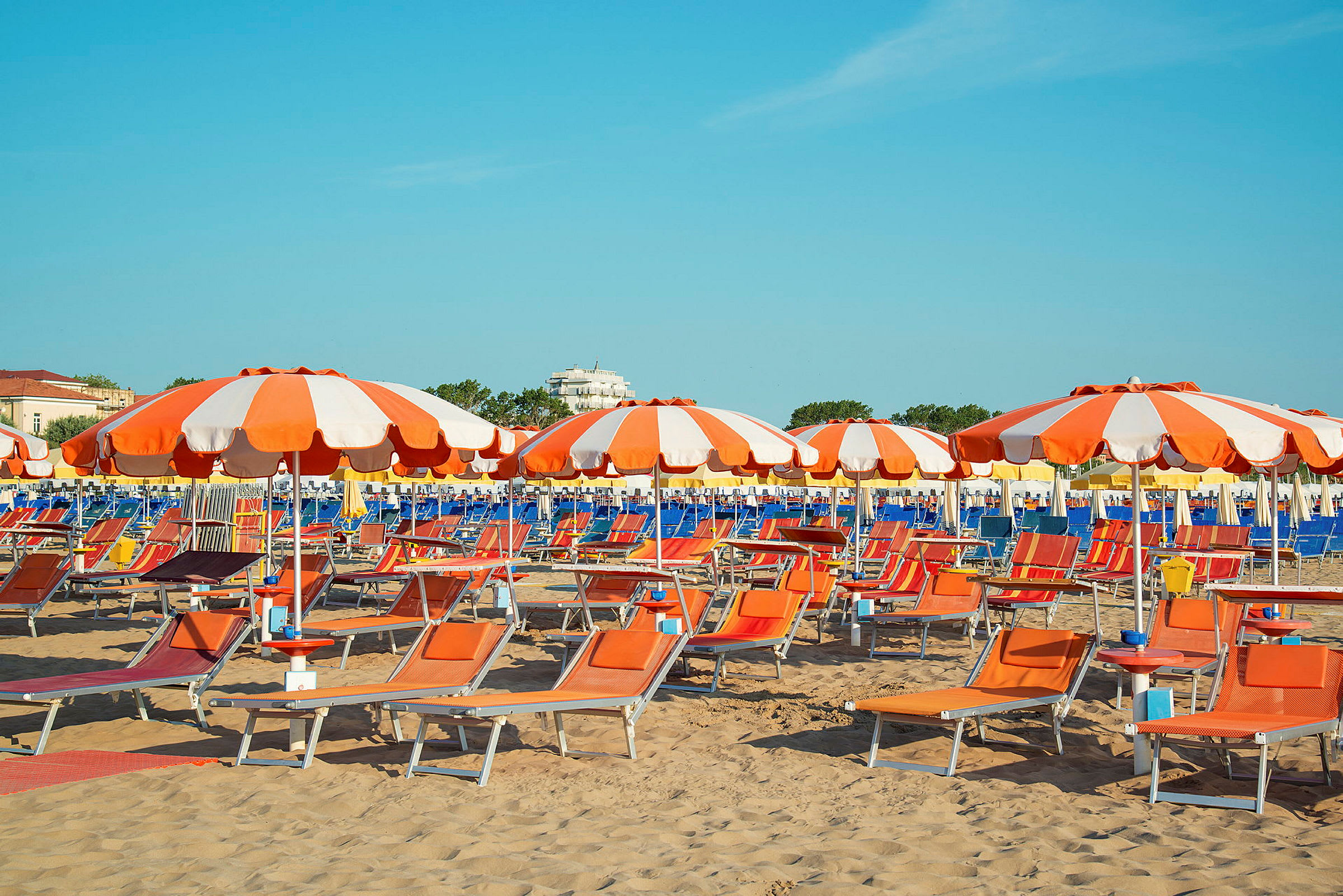 Bild föreställande en sandstrand med orange och vita parasoller samt solstolar. (AI-genererad text)