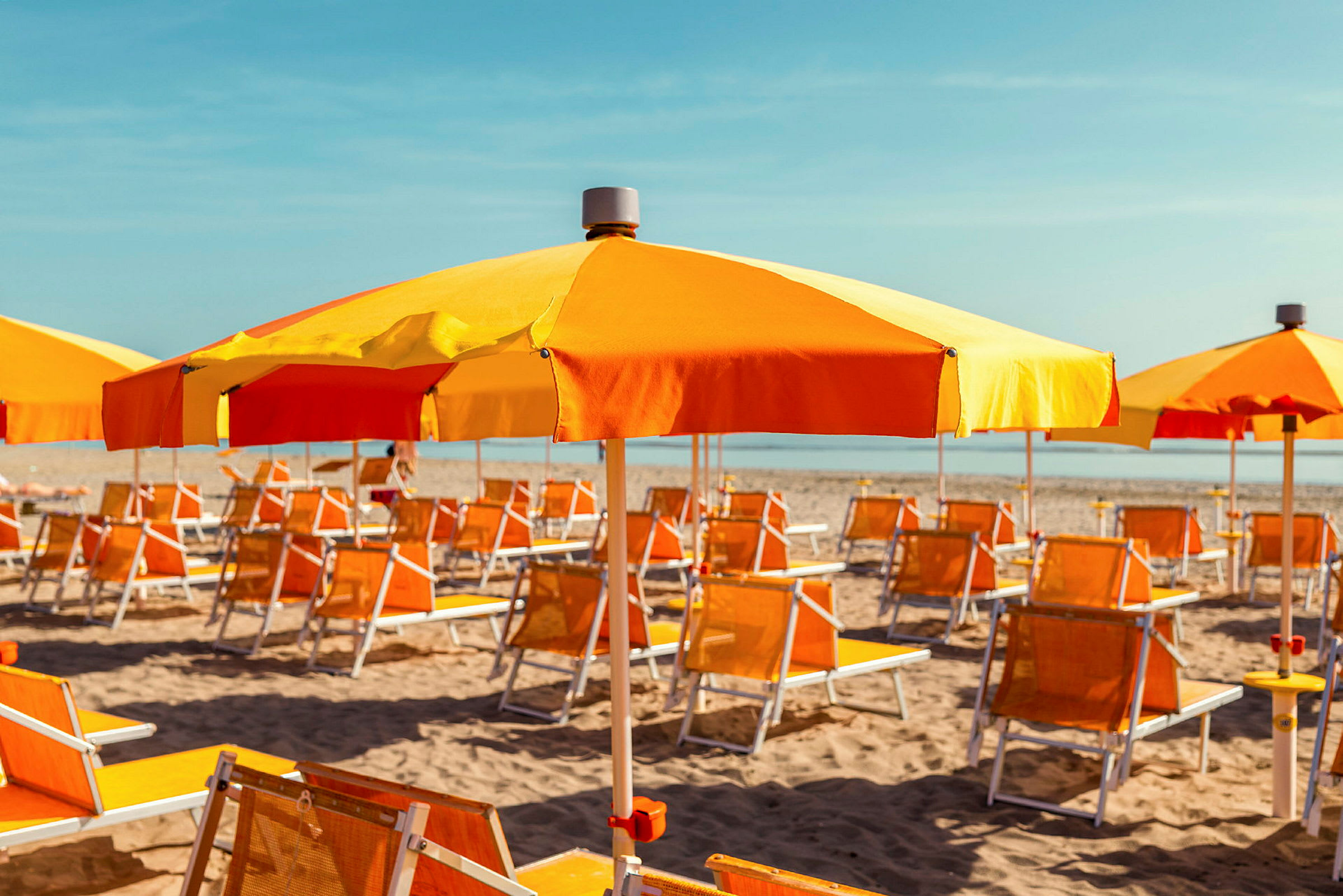 Solstolar och parasoller i orange och gult står uppradade på en sandstrand. (AI-genererad text)