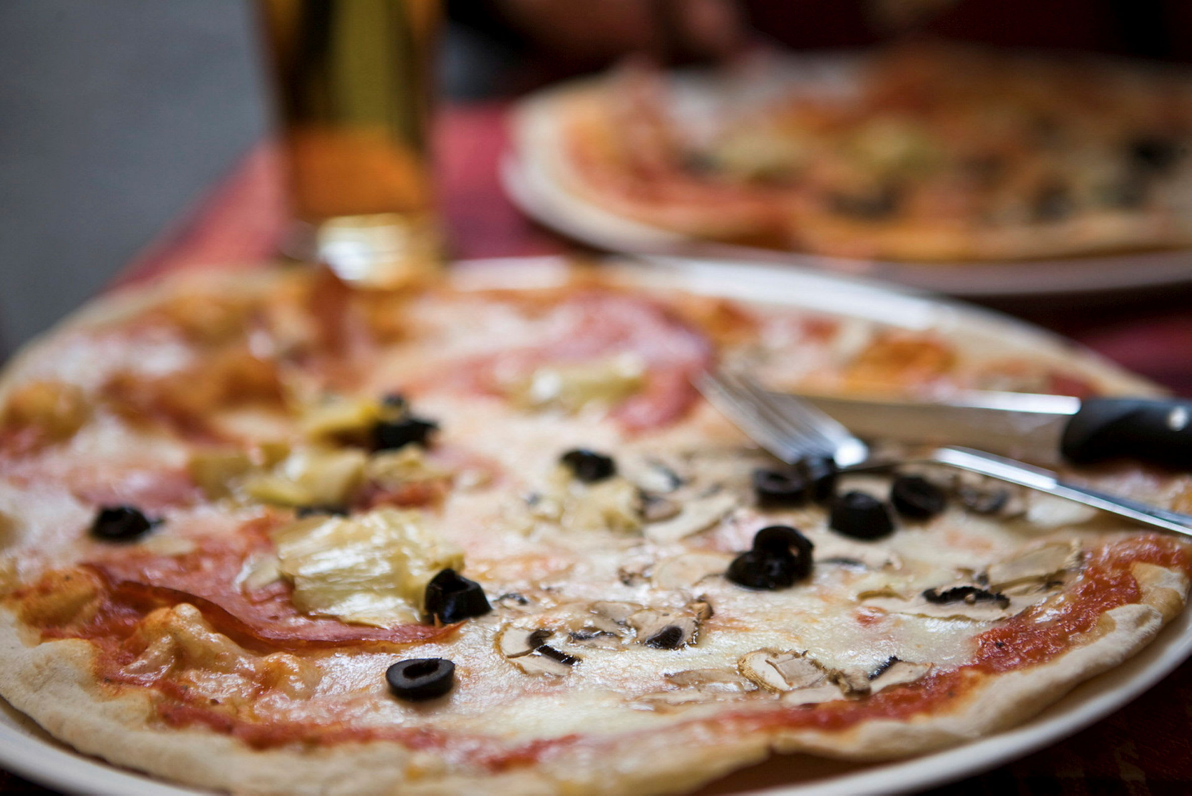 En tallrik med pizza toppad med ost, svarta oliver och champinjoner. Bestick ligger på kanten av tallriken. (AI-genererad text)