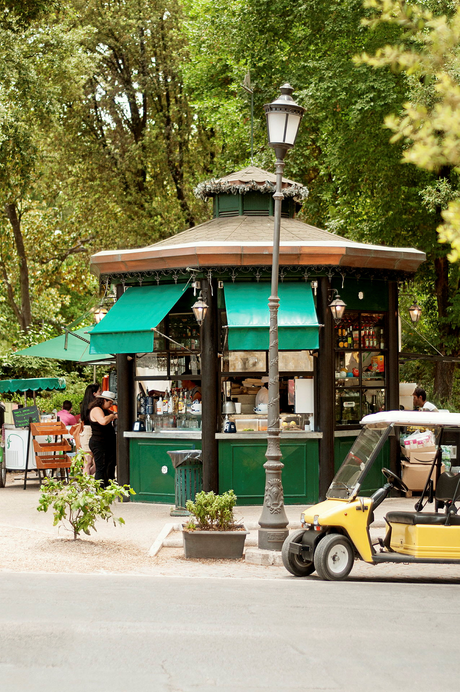 Grön kiosk med markiser och omgivande träd, en gul golfbil syns nära. (AI-genererad text)
