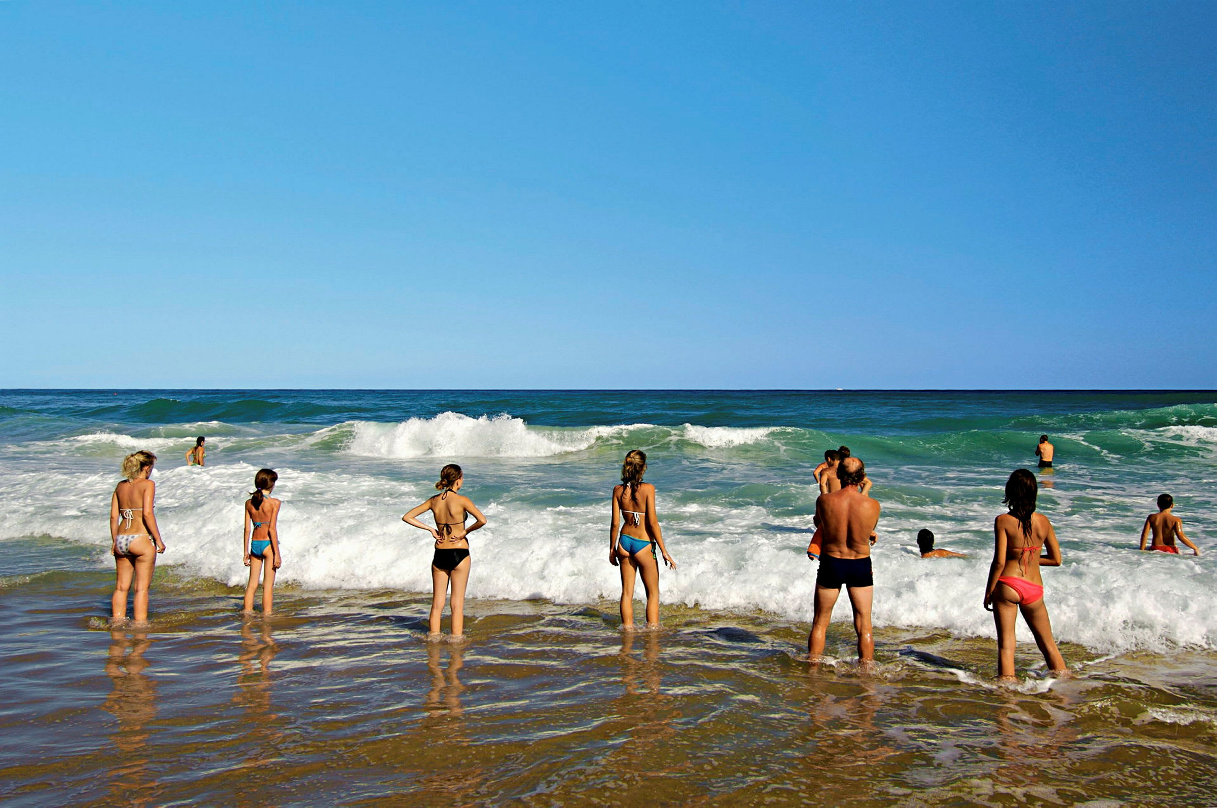 Människor står på en strand och tittar ut över vågorna i havet. (AI-genererad text)