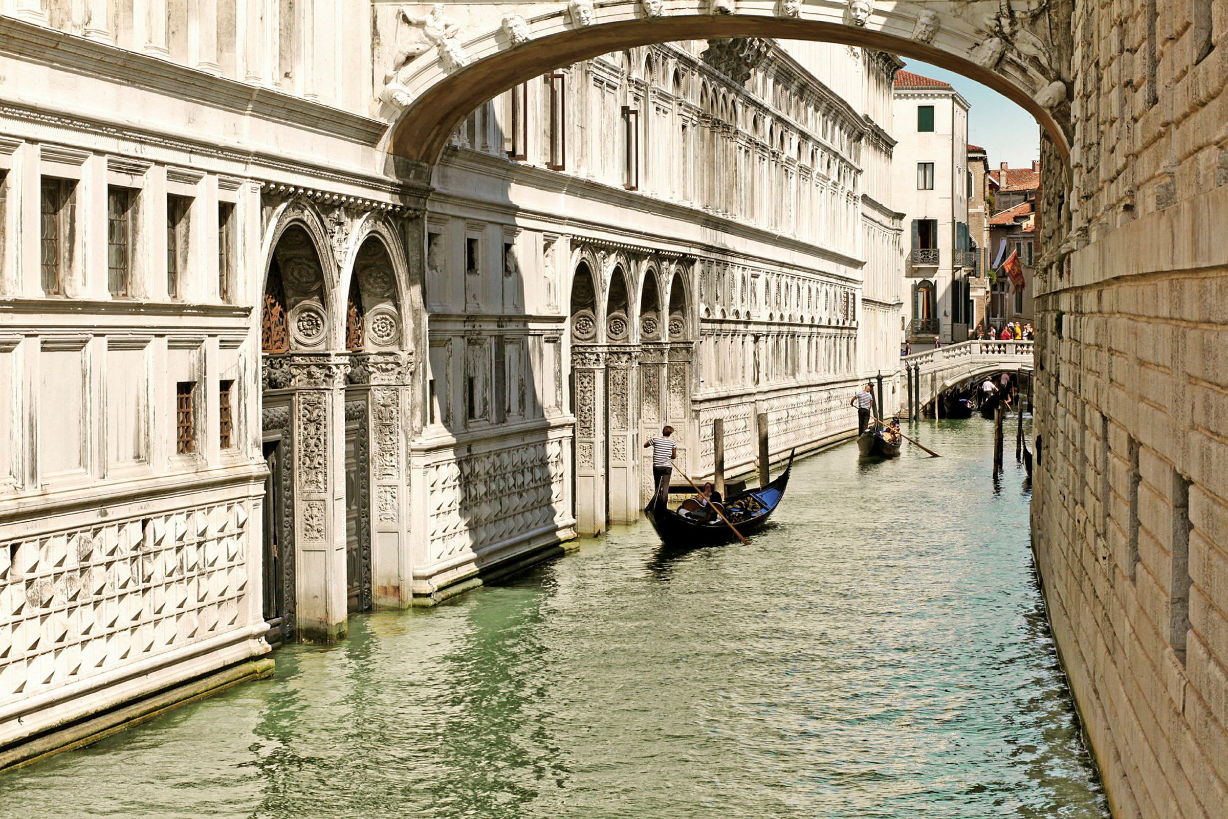 En gondol färdas längs en kanal i Venedig, omgivet av historiska byggnader och en liten bro. (AI-genererad text)
