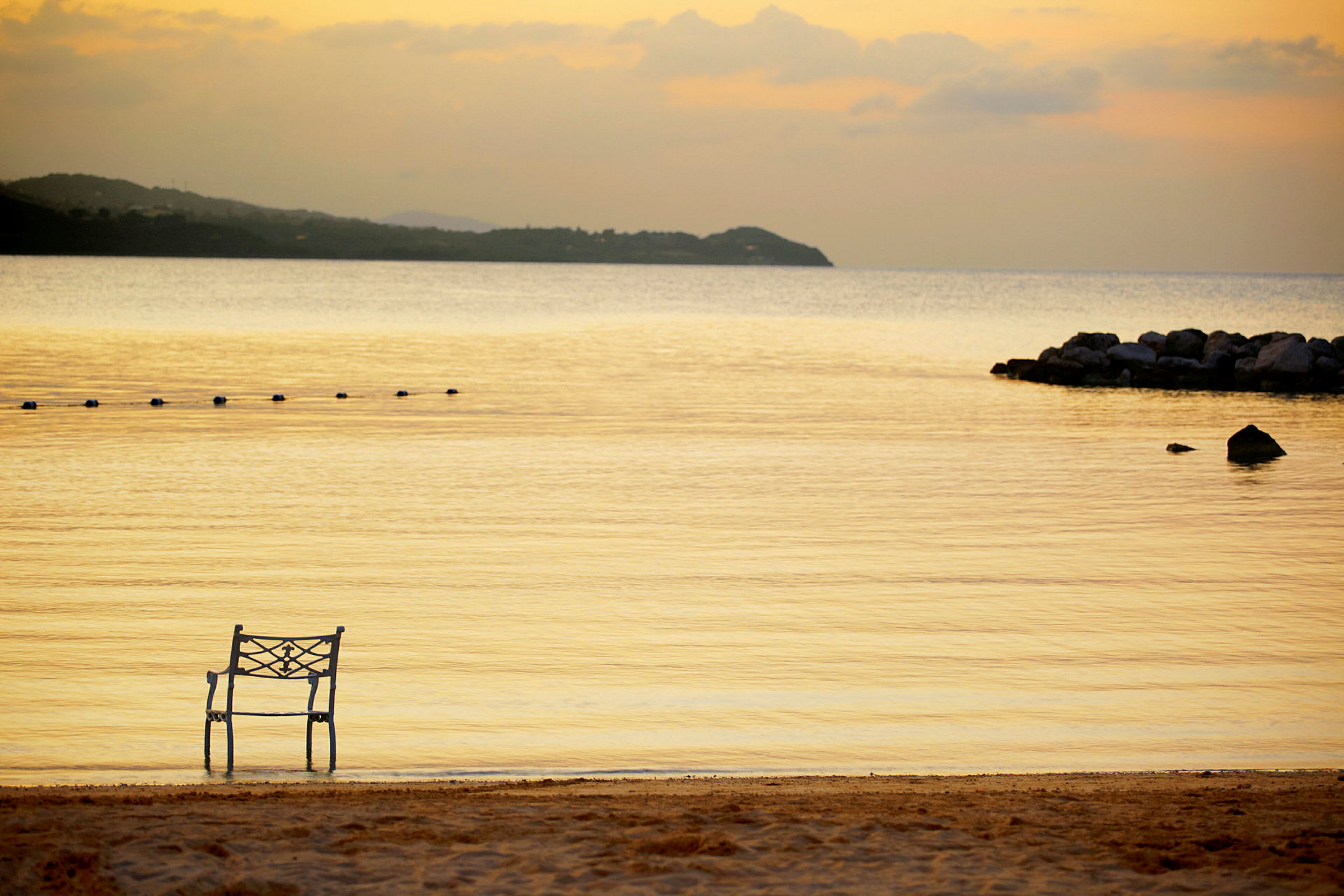 En stol placerad vid stranden med stilla vatten och en solnedgång i bakgrunden. (AI-genererad text)
