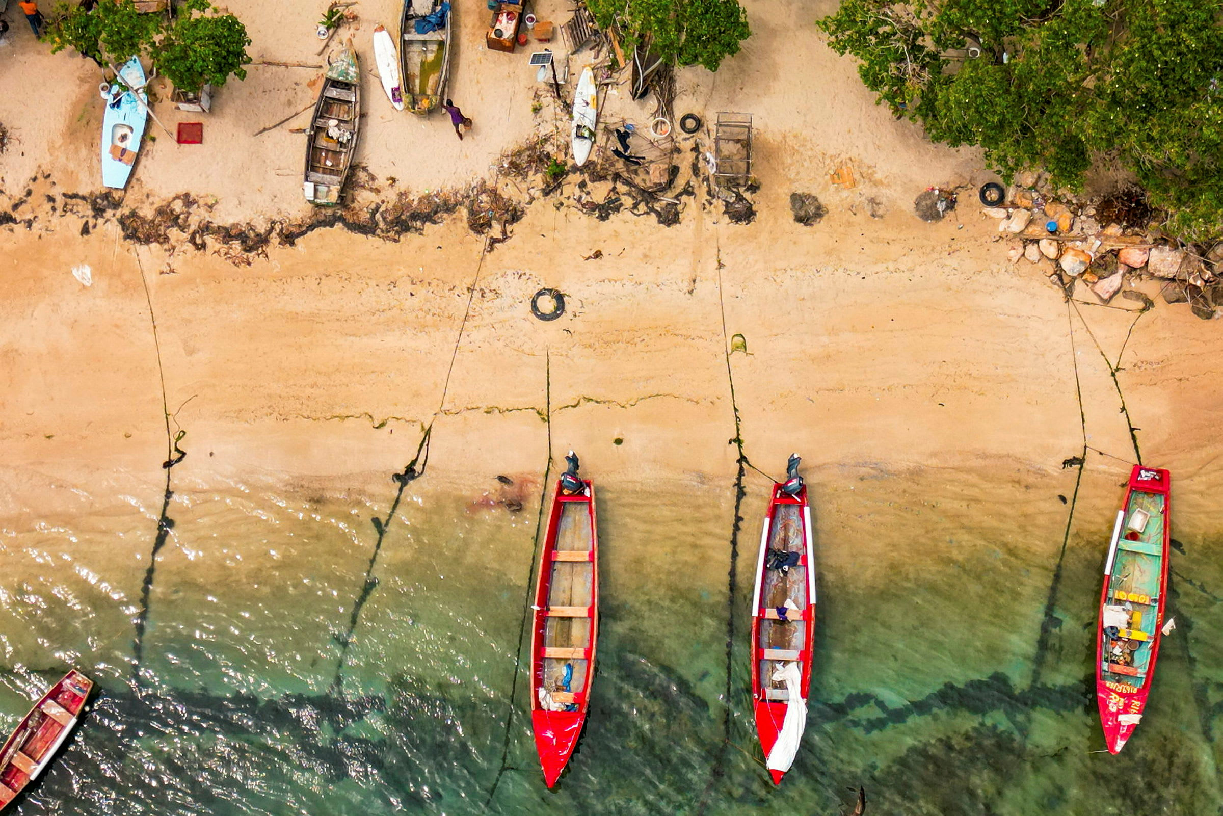 Flera små båtar ligger förtöjda vid en sandstrand med klart vatten. (AI-genererad text)