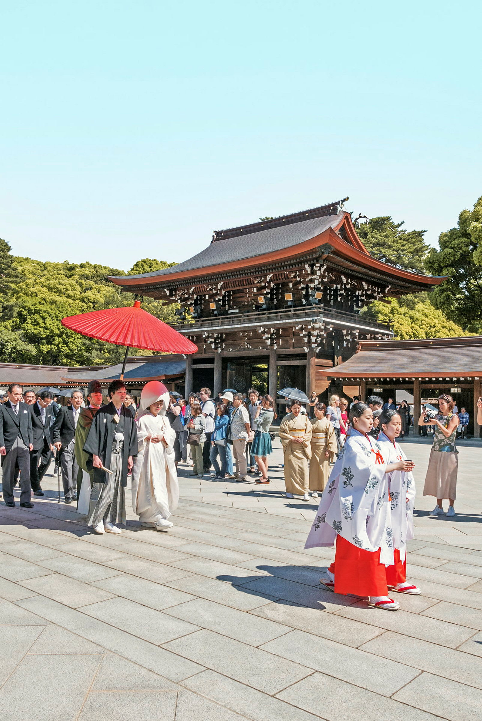 En traditionell ceremoni vid en japansk helgedom, med personer i traditionella kläder och en byggnad med rött tak i bakgrunden. (AI-genererad text)
