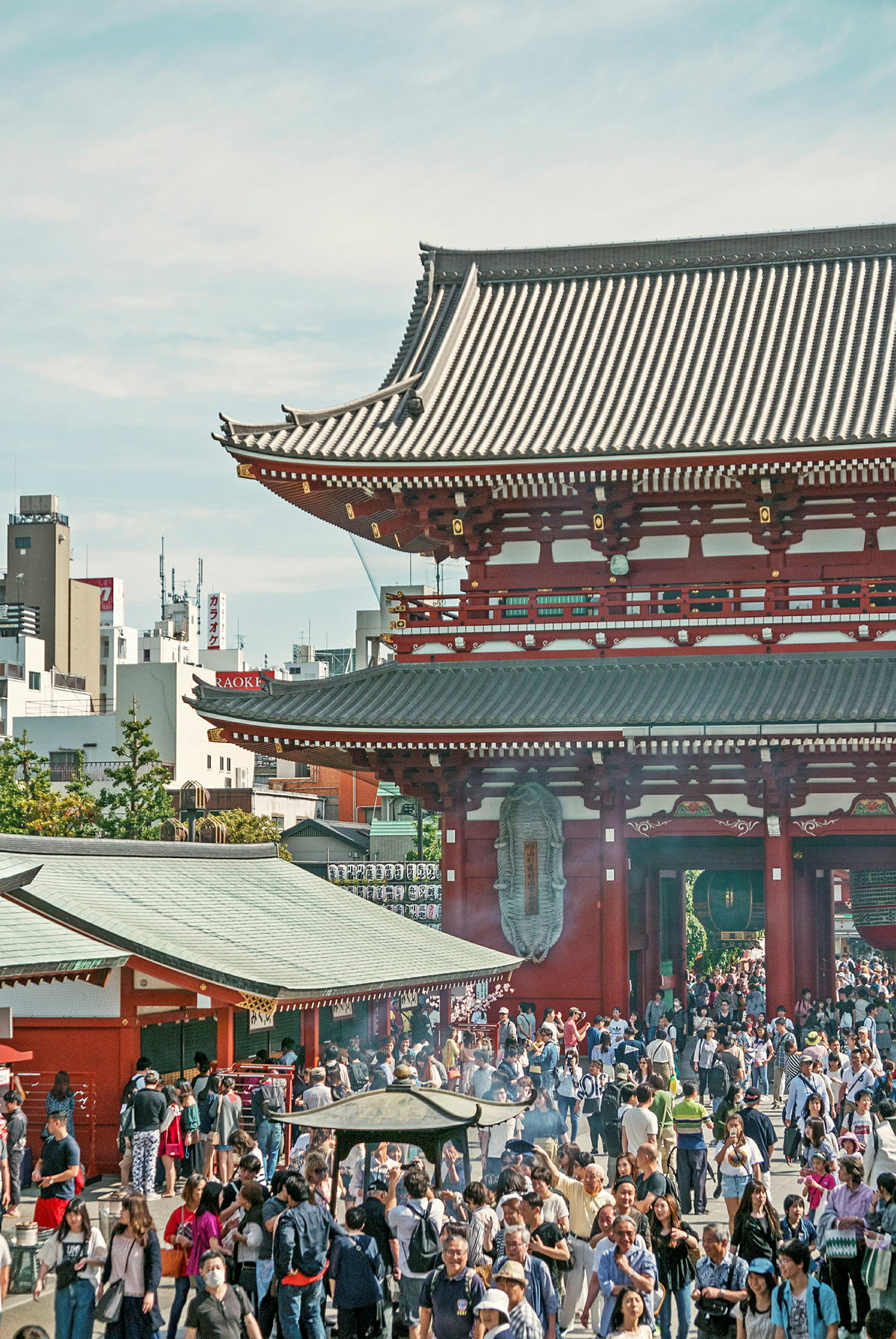 En folkmassa samlad framför en traditionell japansk byggnad med röd fasad och detaljerad arkitektur. (AI-genererad text)
