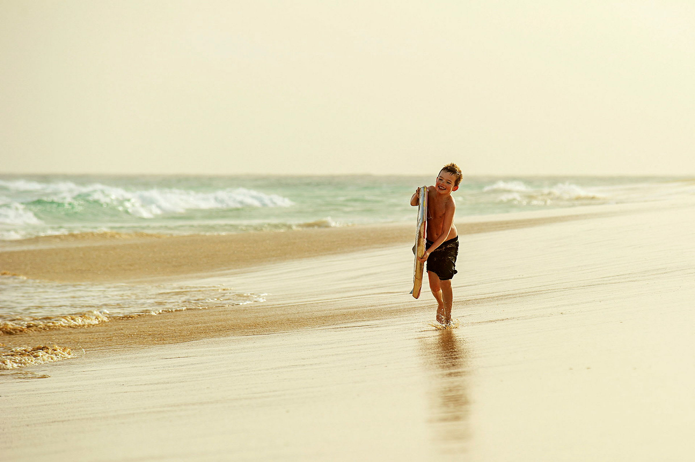 En person på en sandstrand nära havet. Personen bär en surfbräda och går på vattnet. (AI-genererad text)