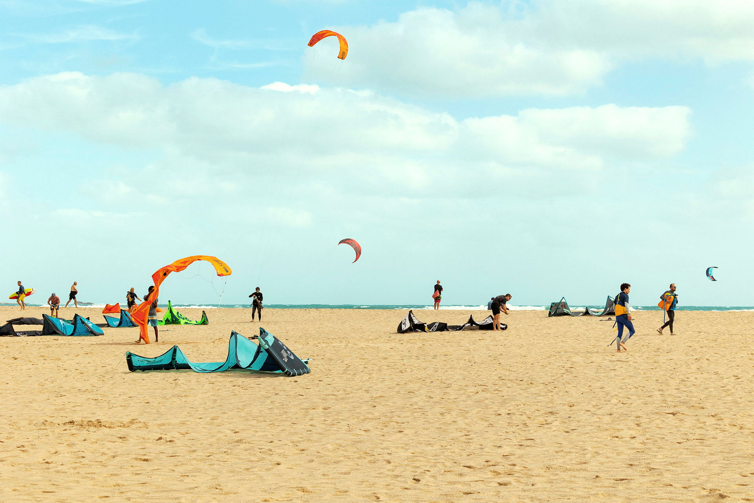 Strand med personer som riggar utrustning för kitesurfing med flygande färgade drakar. (AI-genererad text)