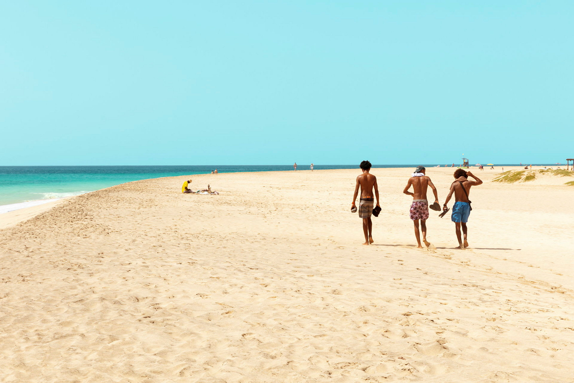 Tre personer promenerar på en sandstrand nära havet. (AI-genererad text)