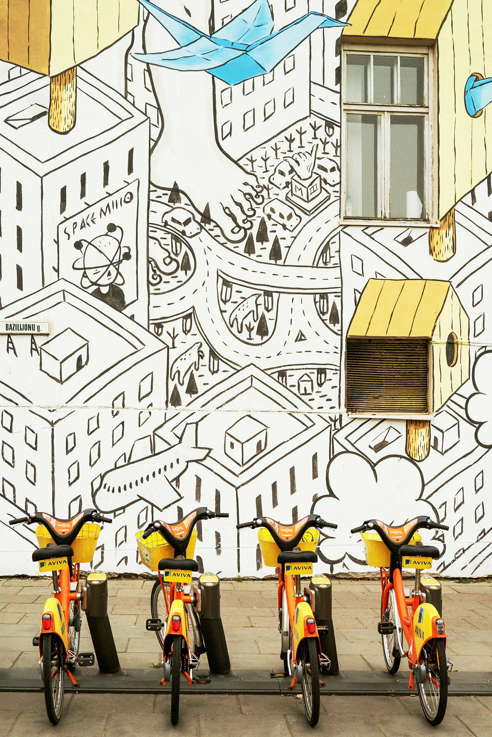 En rad med gul-orange cyklar framför en vägg med illustrerat stadslandskap. (AI-genererad text)