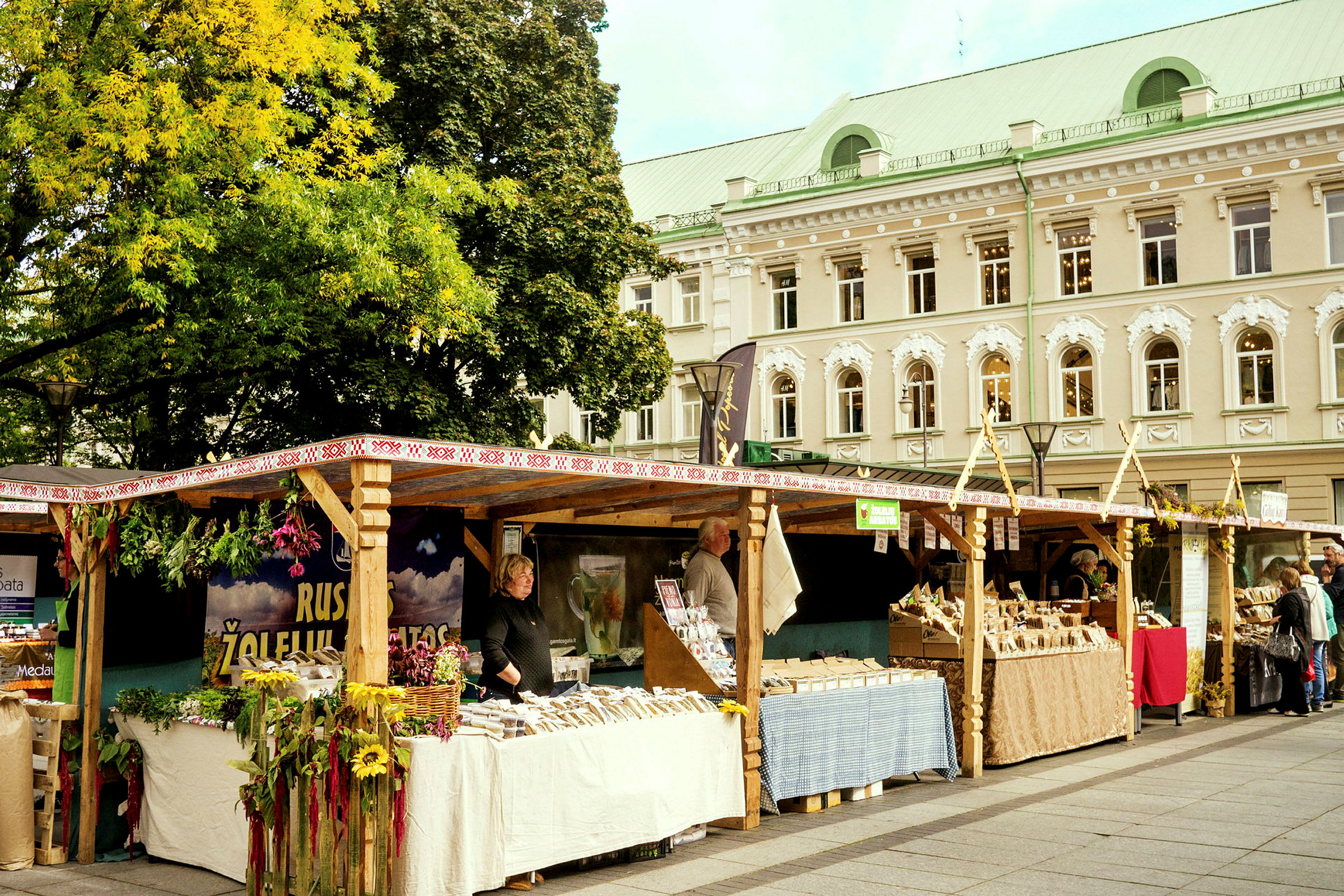 Ett torg med marknadsstånd fyllda med varor och dekorationer. En byggnad syns i bakgrunden. (AI-genererad text)