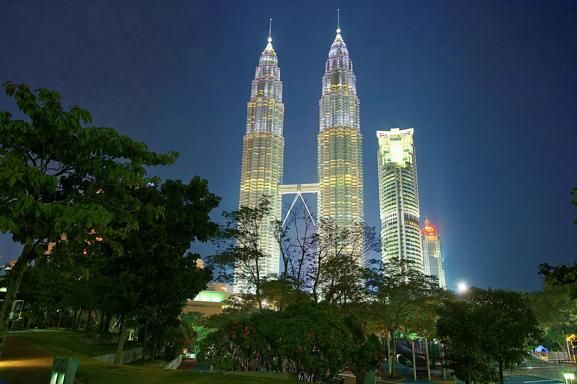 Petronas Twin Towers upplysta på natten med träd i förgrunden. (AI-genererad text)