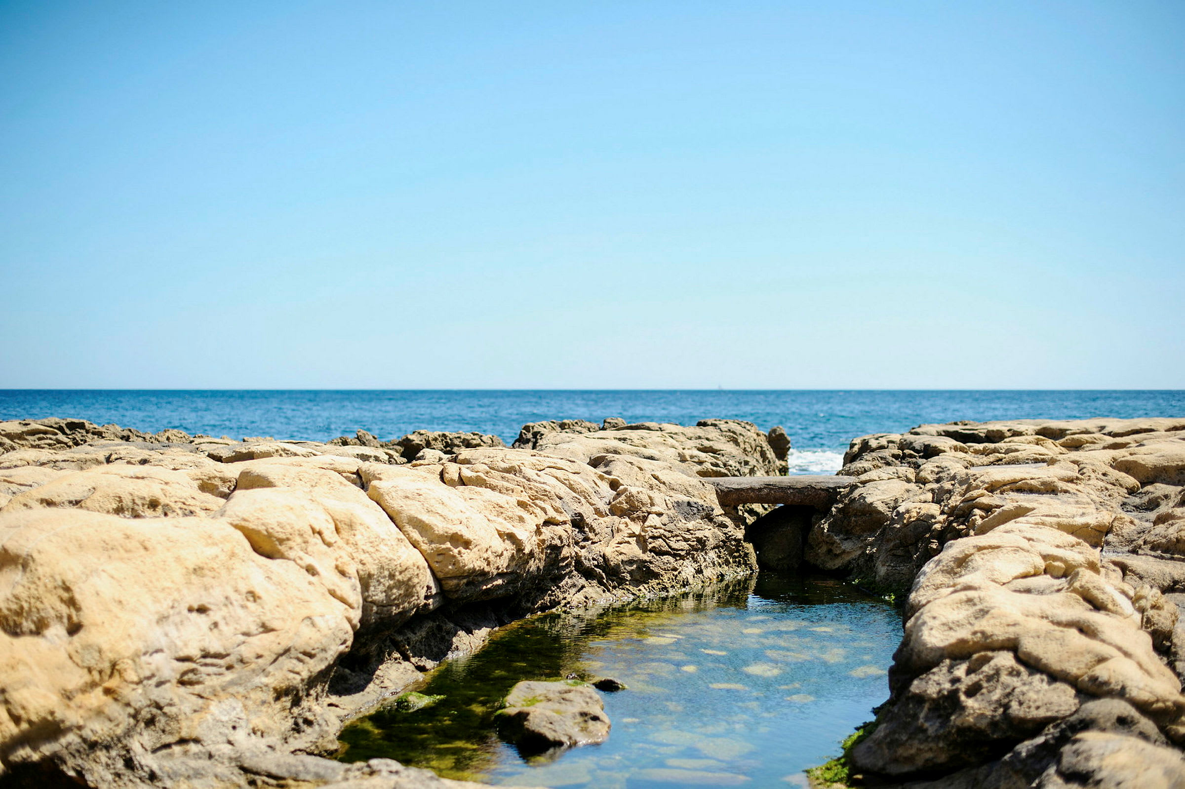 En klippformation med en liten vattenpöl och havet i bakgrunden. (AI-genererad text)