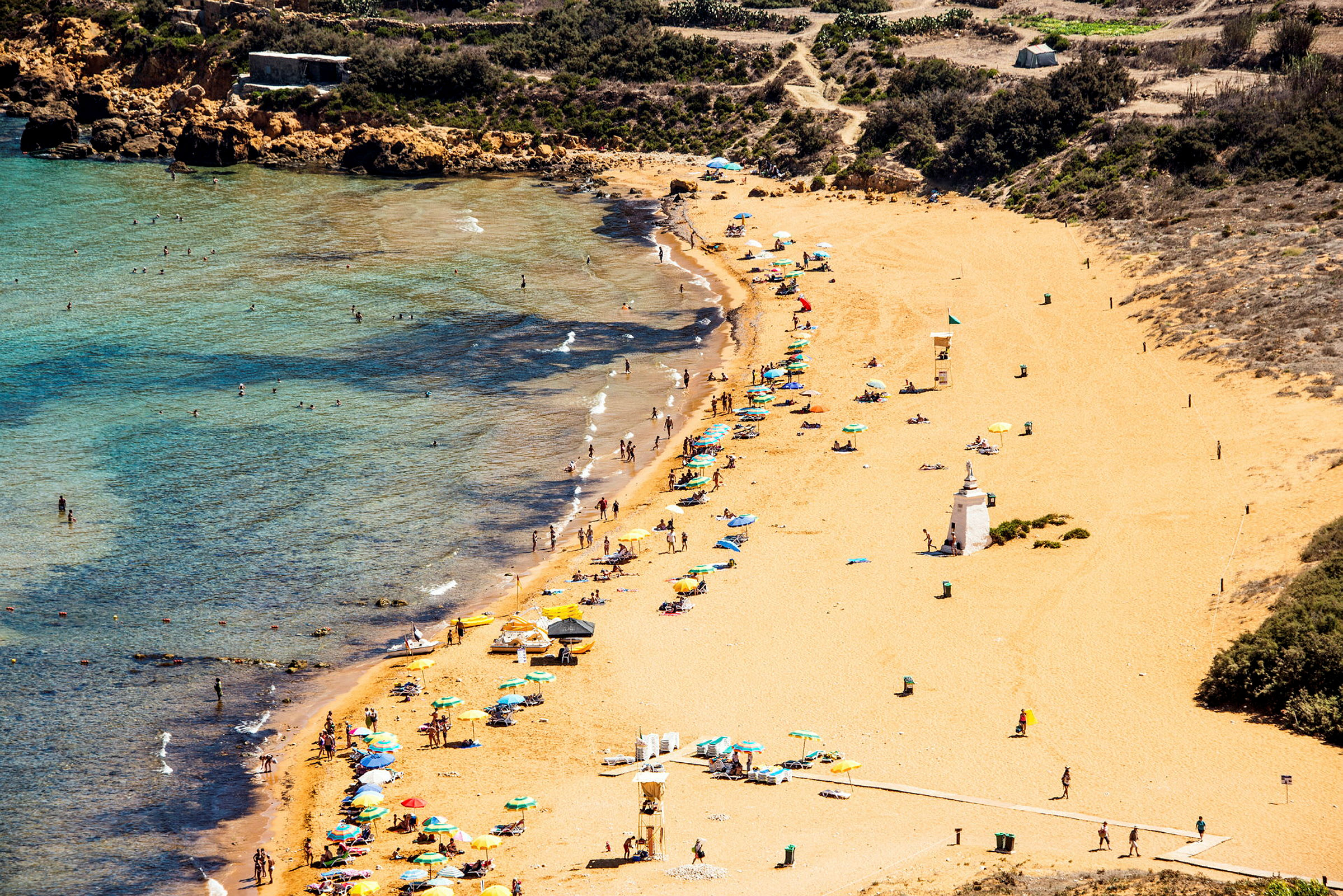 En strand med gyllene sand, parasoller och badande personer i vattnet. (AI-genererad text)