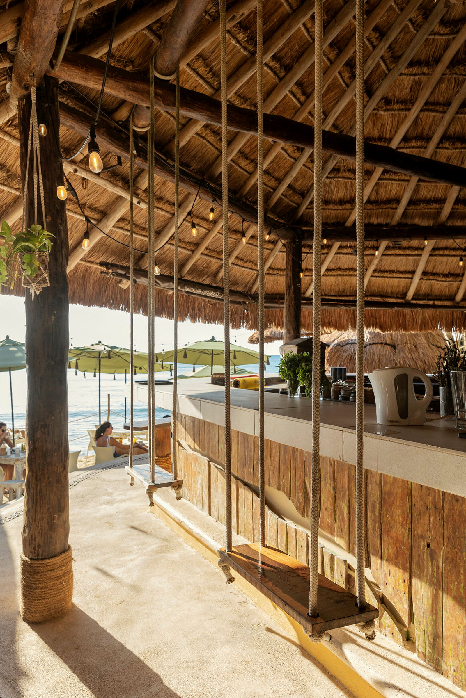 Interiör av en strandbar med gungor vid bardisken och halmtak. (AI-genererad text)