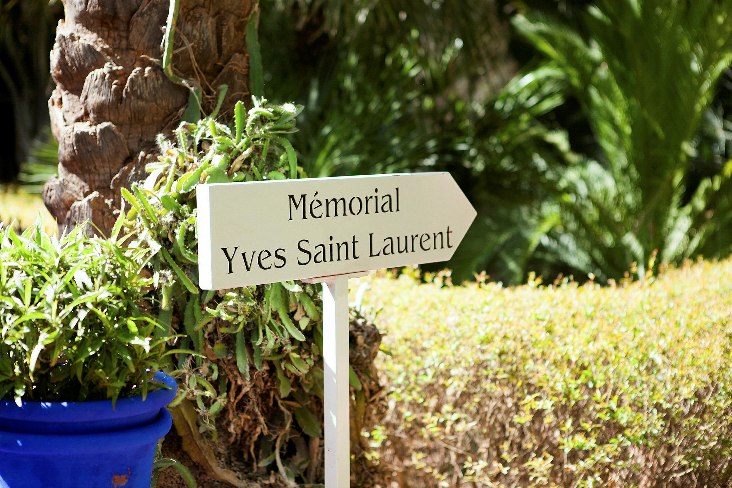 En skylt märkt 'Mémorial Yves Saint Laurent' vid en trädgård med grönska. (AI-genererad text)