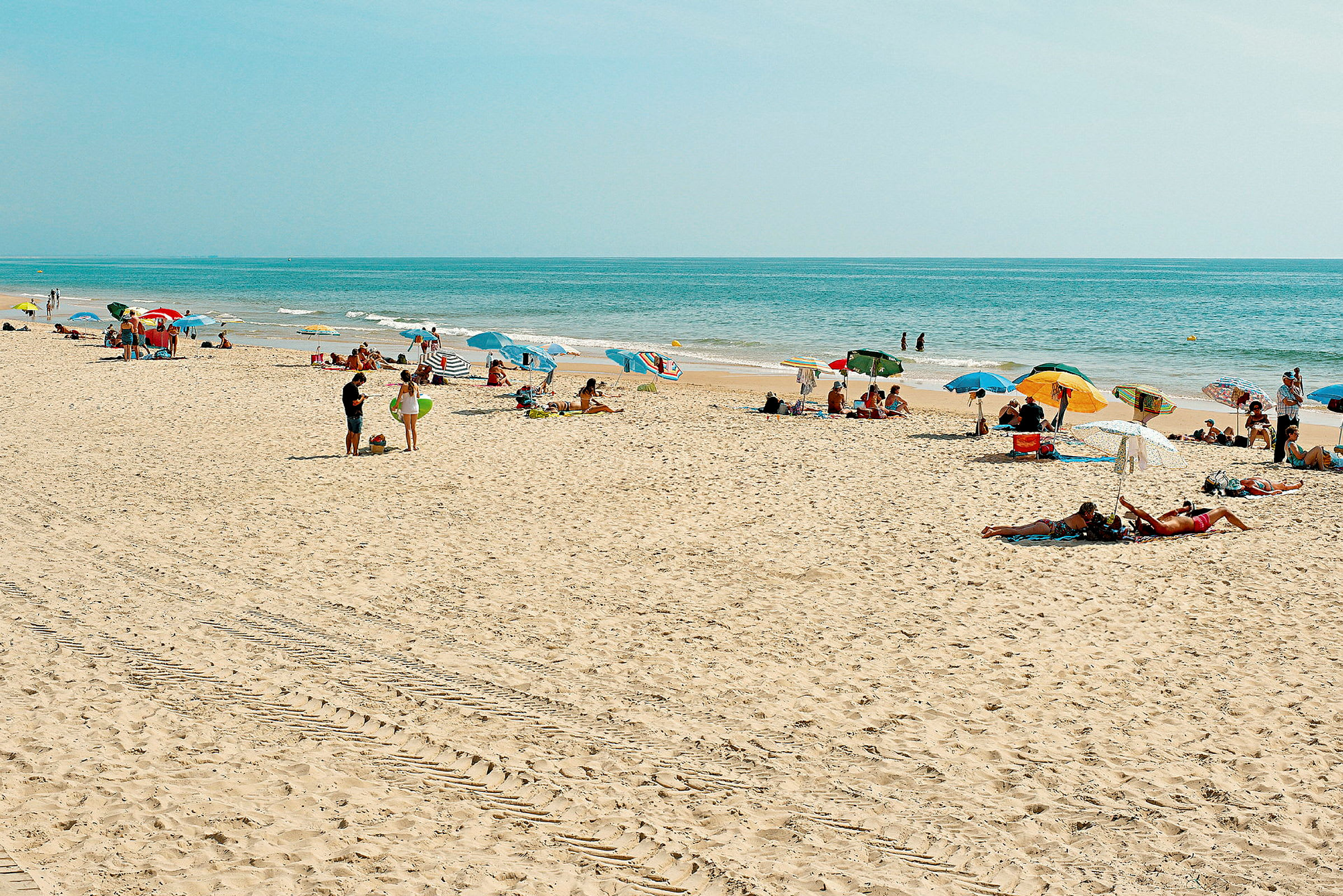 En strand med människor som solar och använder färgglada parasoller. (AI-genererad text)