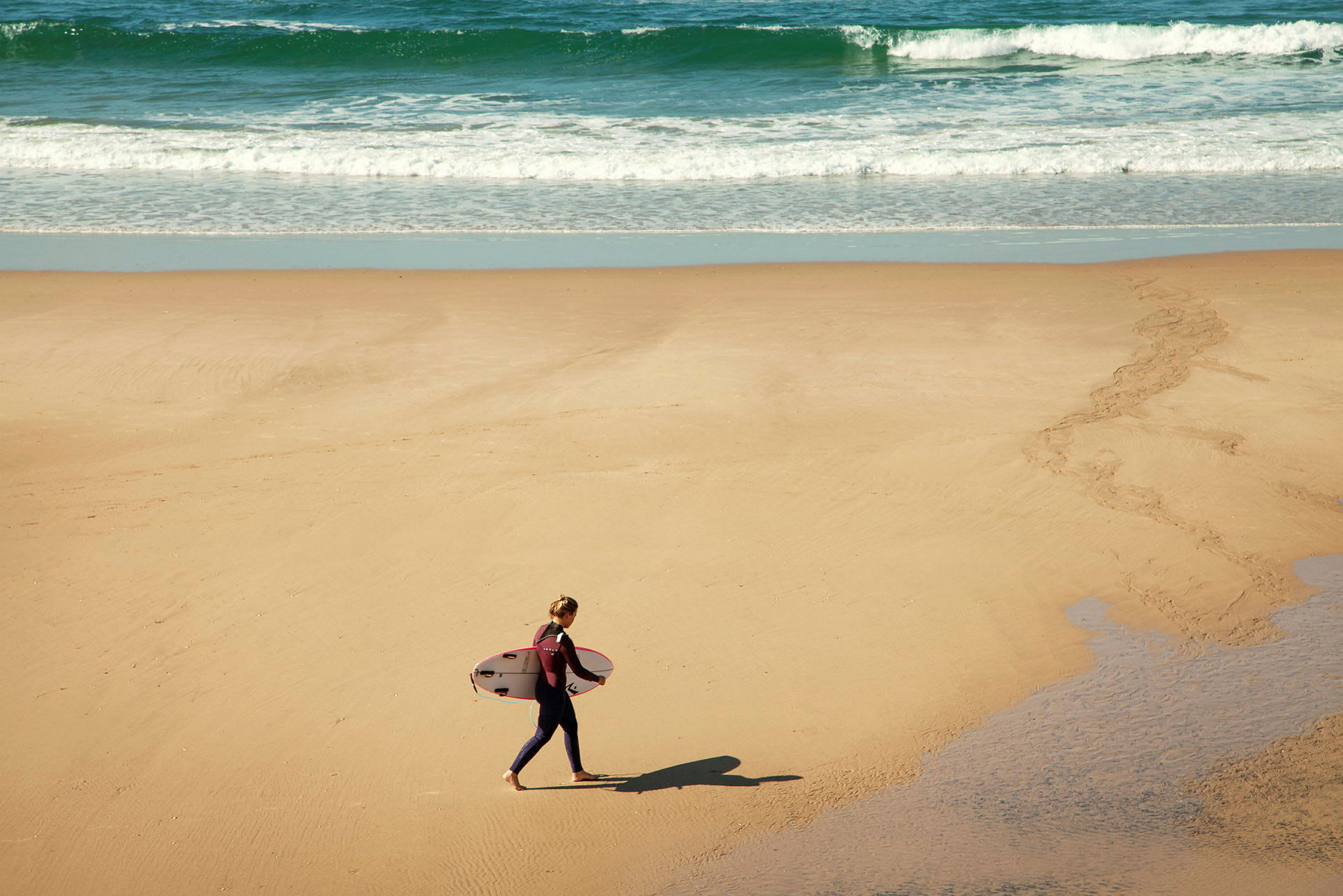 Person går över en sandstrand och bär en surfbräda. (AI-genererad text)