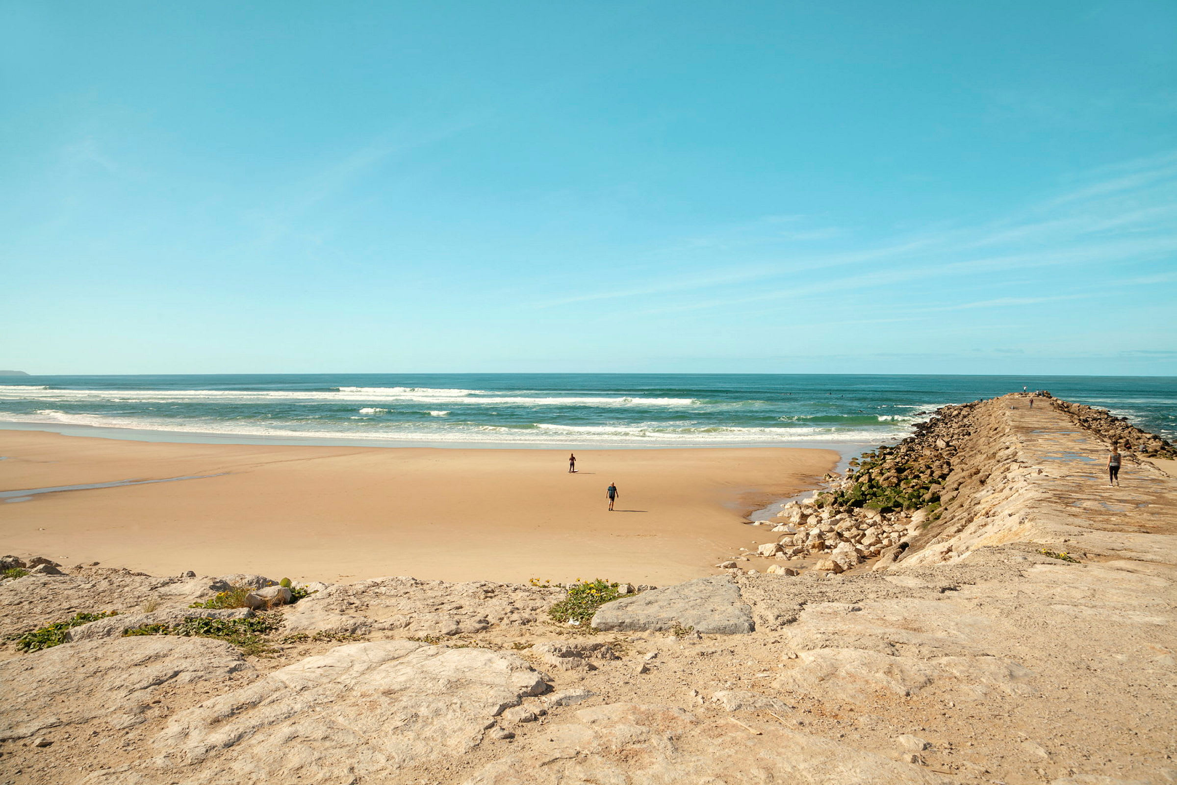 En sandstrand med vatten och en stenbrygga. (AI-genererad text)