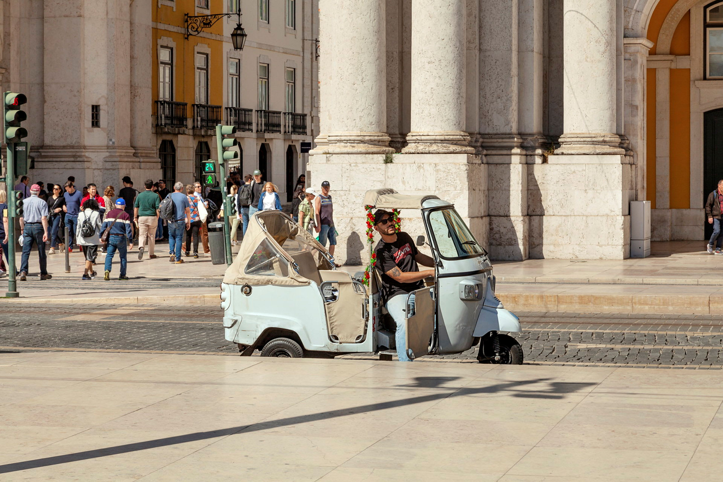 En trehjulig scooter står parkerad framför en byggnad med människor i bakgrunden. (AI-genererad text)