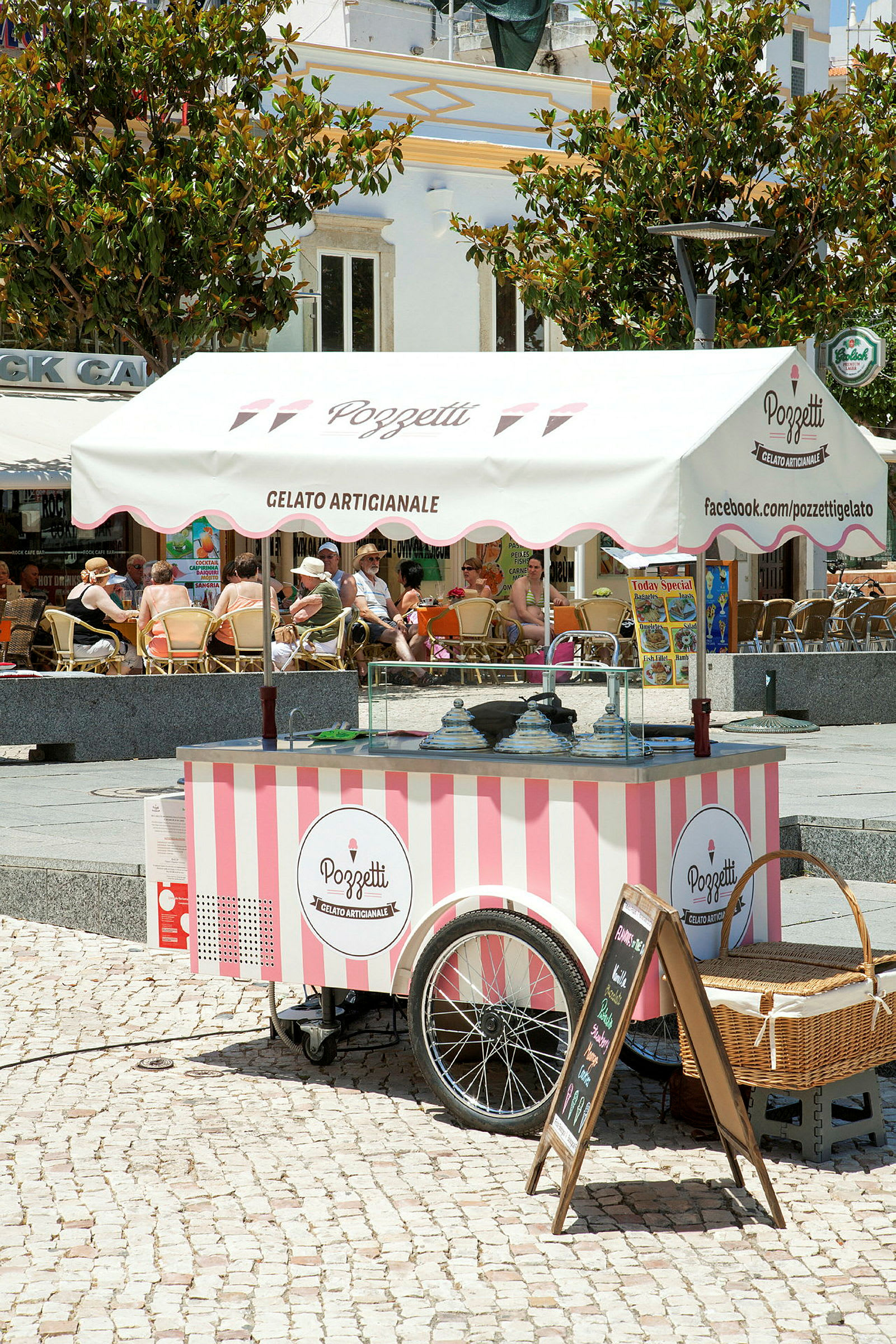 En mobil glasskiosk med rosa och vita ränder under ett tak med texten 'Gelato Artigianale'. (AI-genererad text)
