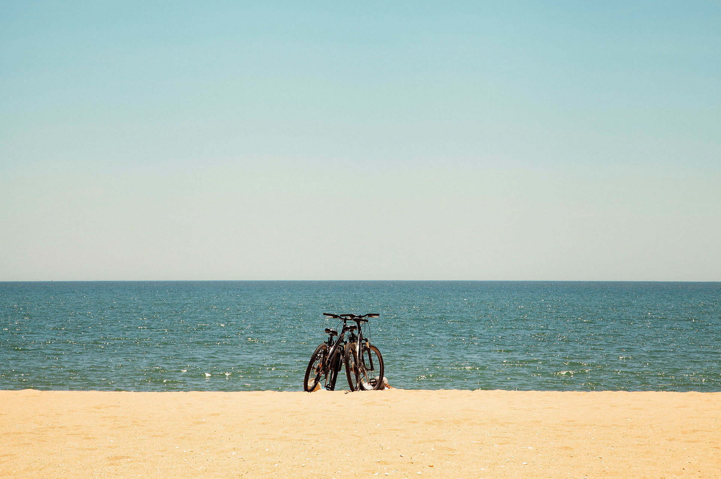 Två cyklar står på en sandstrand med havet i bakgrunden. (AI-genererad text)
