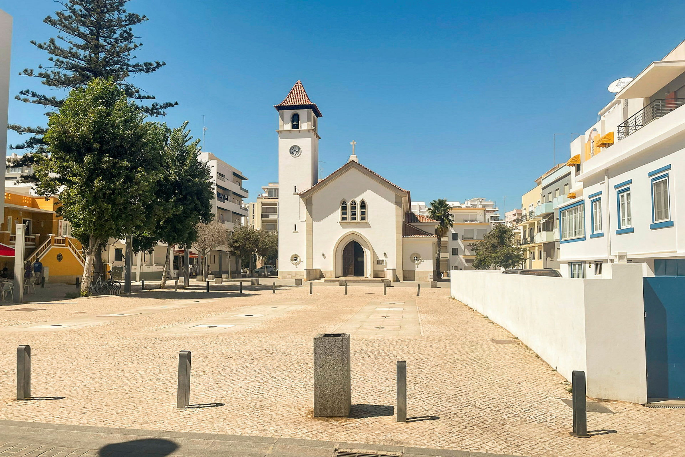En vit kyrka med en klocktorn syns på ett torg omgiven av byggnader. (AI-genererad text)