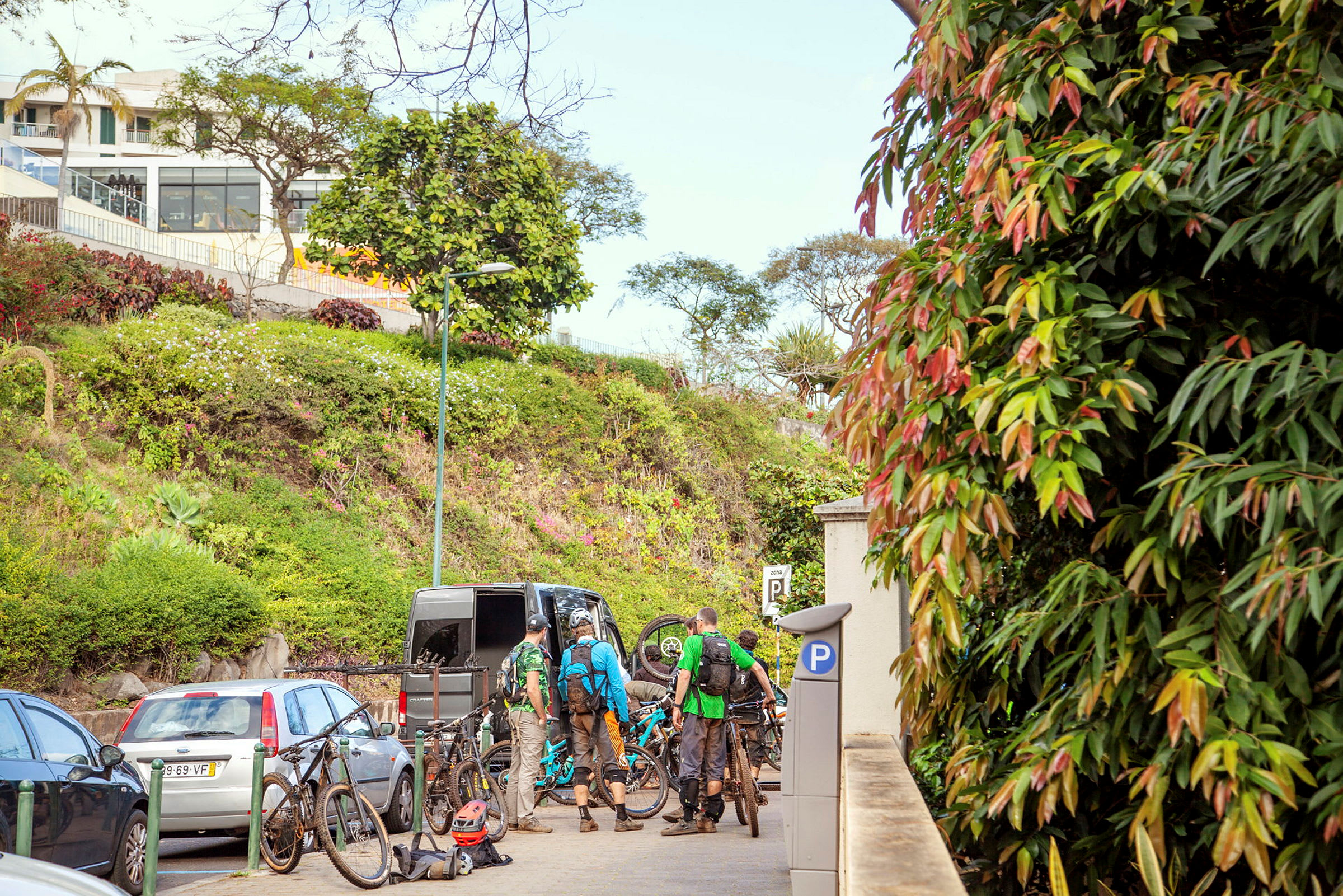 En grupp personer med mountainbikes står vid en parkerad bil nära en grön sluttning. (AI-genererad text)