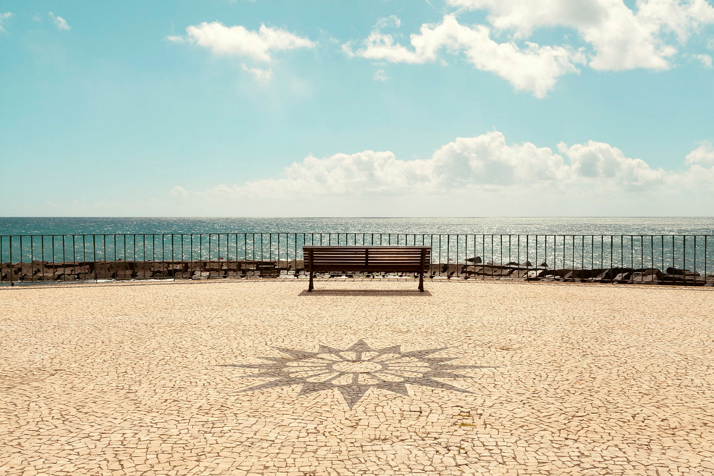 Parkbänk med utsikt över havet, stenläggning och horisont. (AI-genererad text)