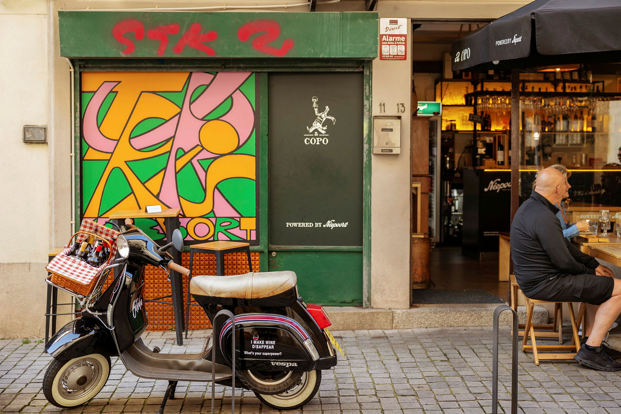 En Vespa med en korg fram för flaskor står parkerad framför en butik med en färgglad väggmålning. (AI-genererad text)