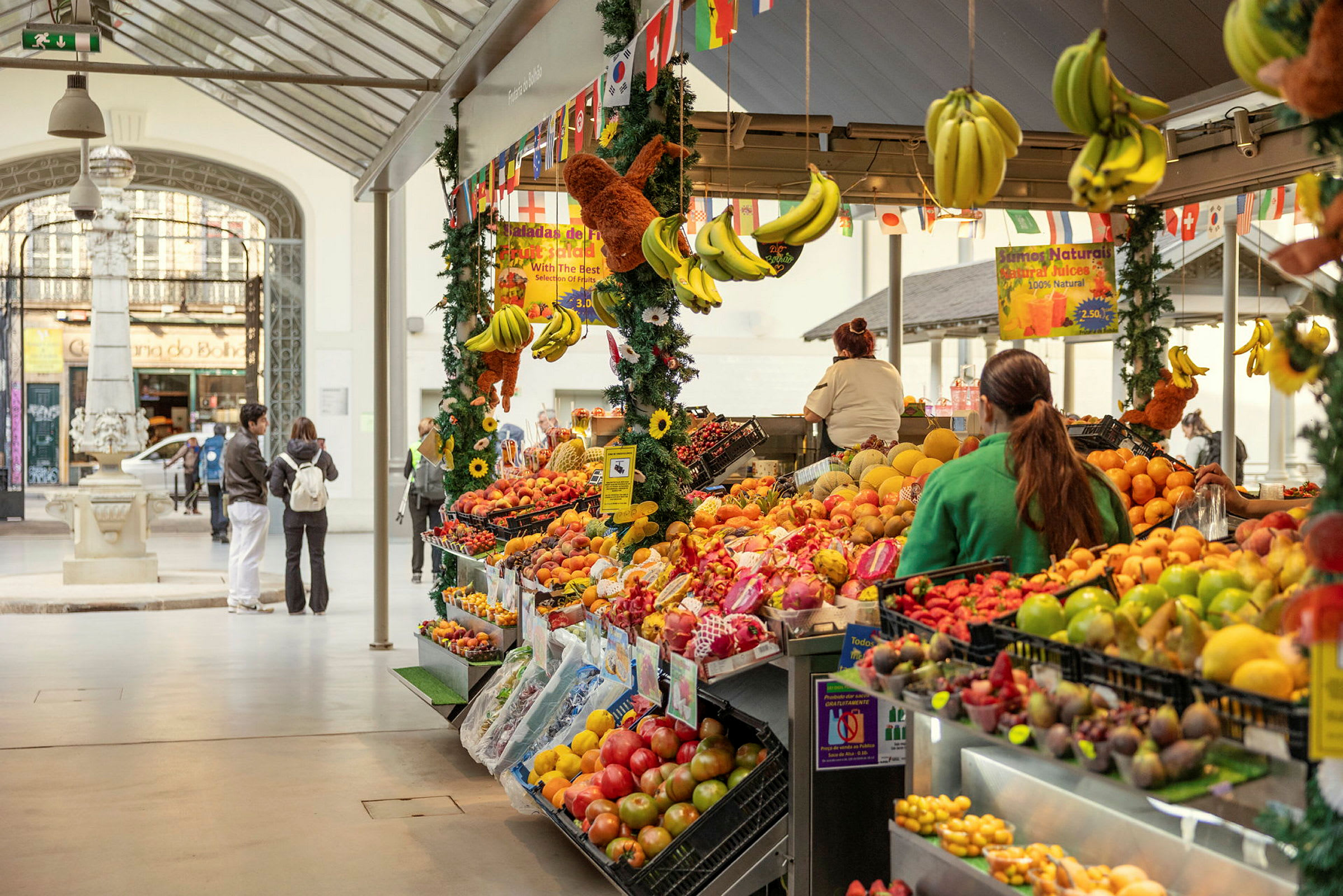 En marknadsstånd displayar färgglada frukter med bananer hängande ovanför. (AI-genererad text)