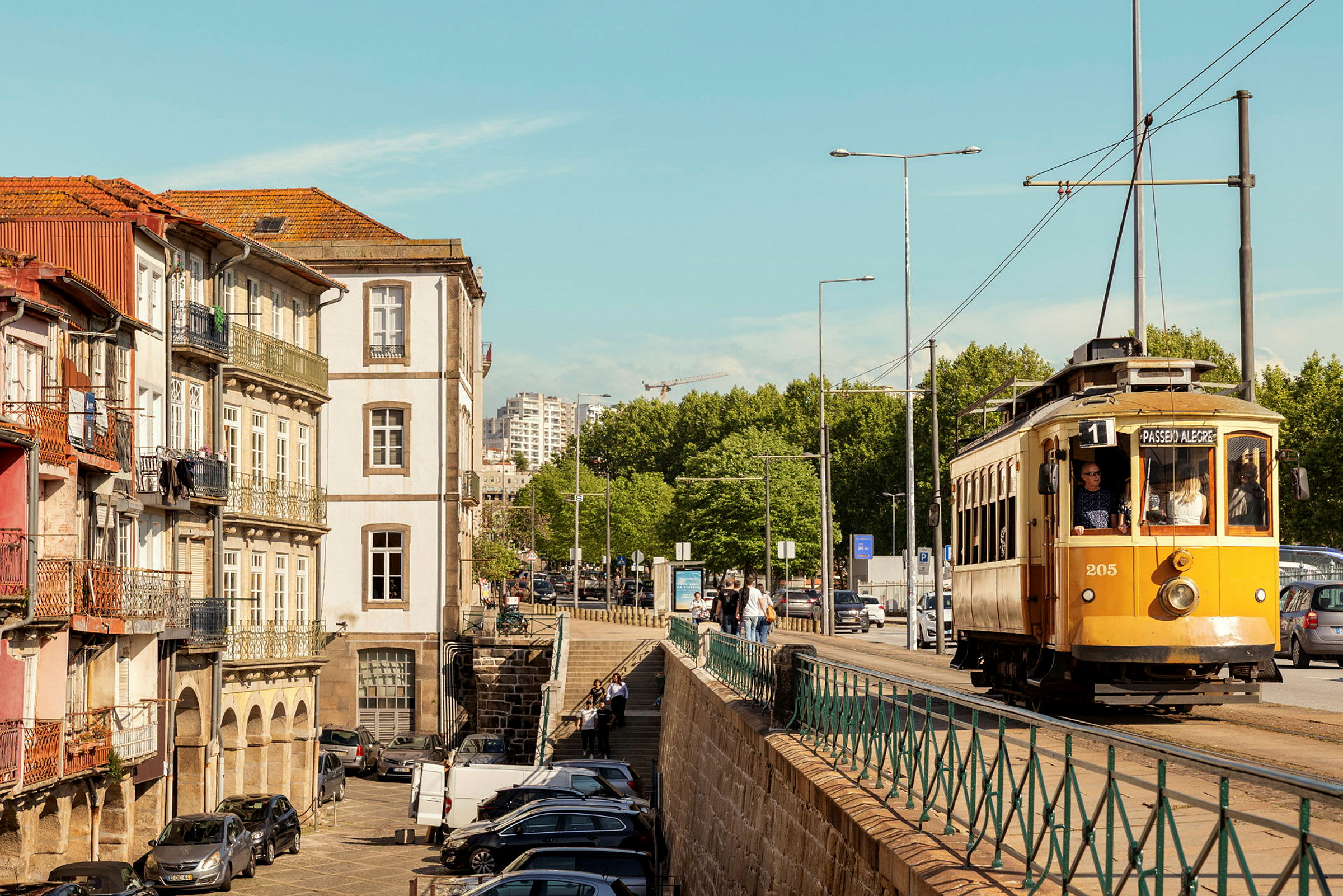 En gul spårvagn kör längs en gata omgiven av klassiska byggnader och grönska. (AI-genererad text)