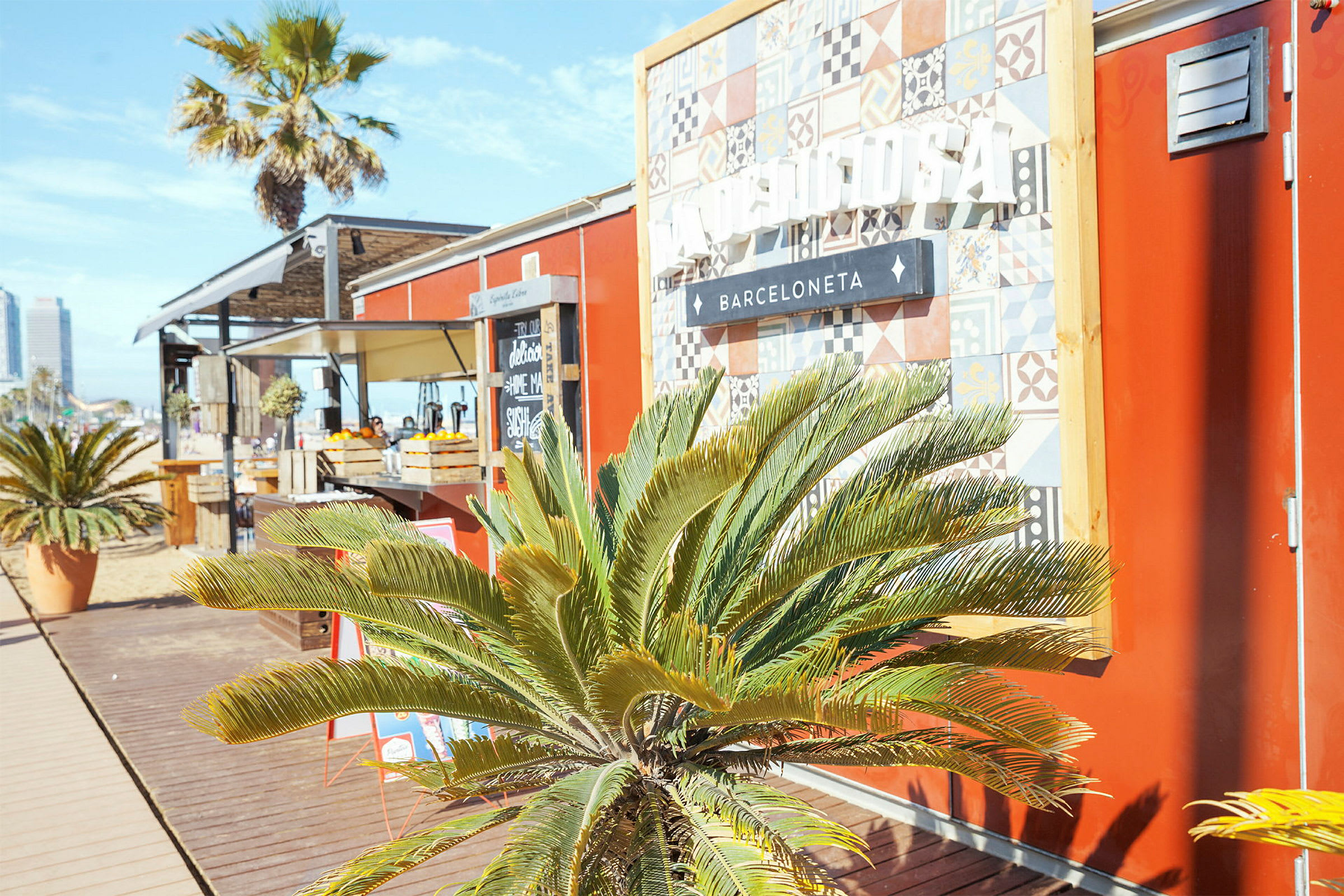 En liten strandbar med röda väggar, en dekorativ skylt och gröna palmväxter framför. (AI-genererad text)