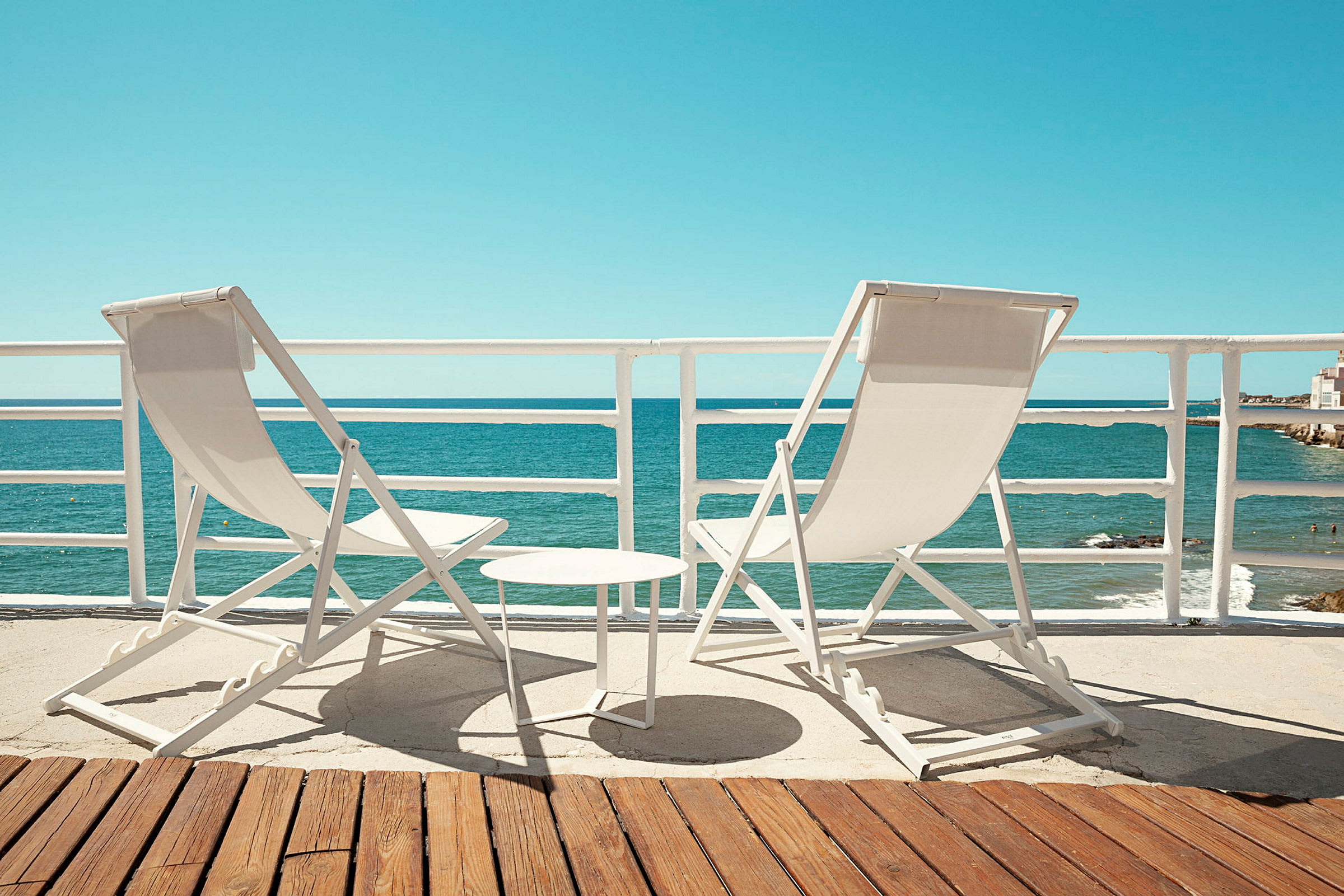Två solstolar och ett litet bord står på en terrass med utsikt över havet. (AI-genererad text)