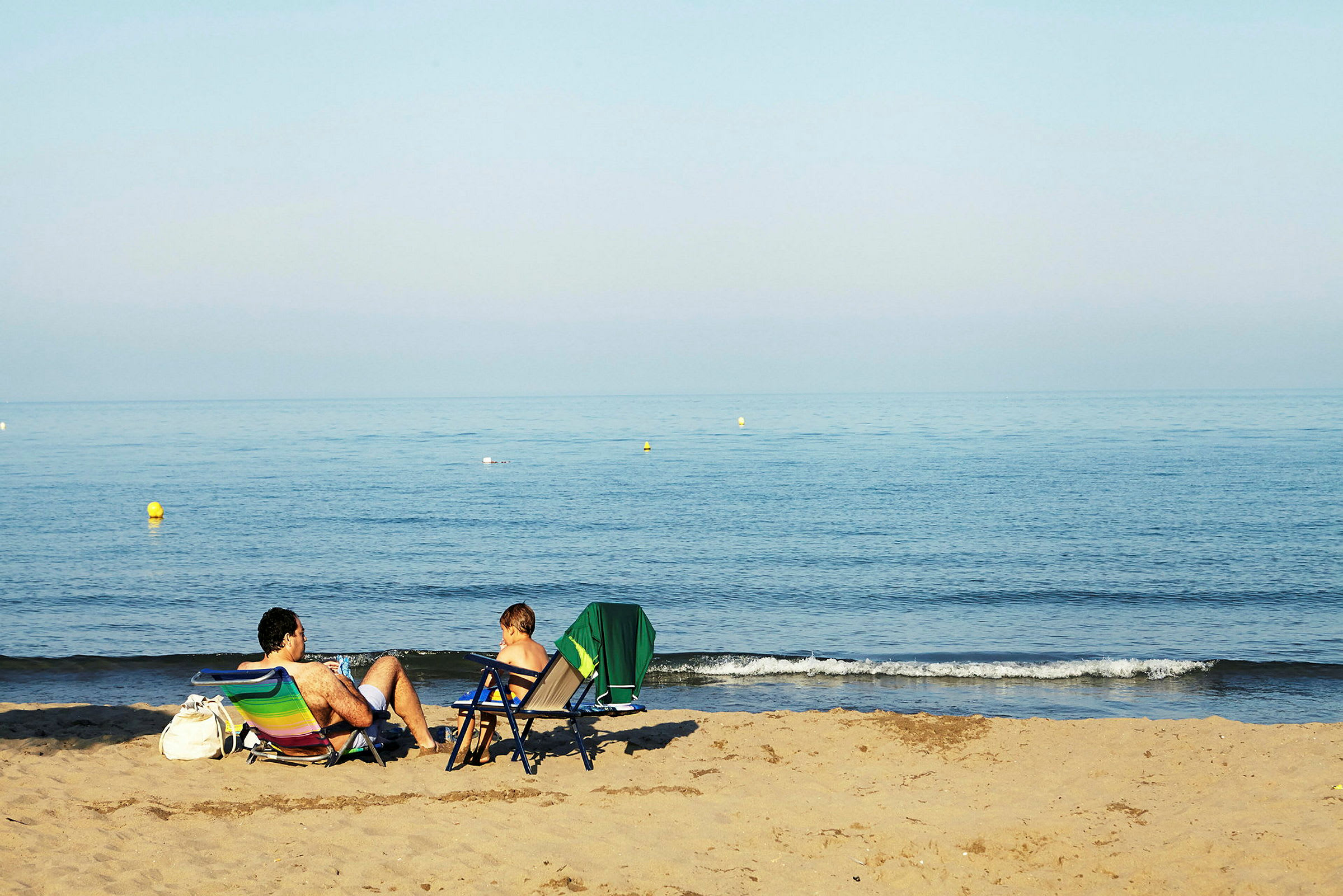 Två personer sitter i strandstolar på en sandstrand och tittar på havet. (AI-genererad text)