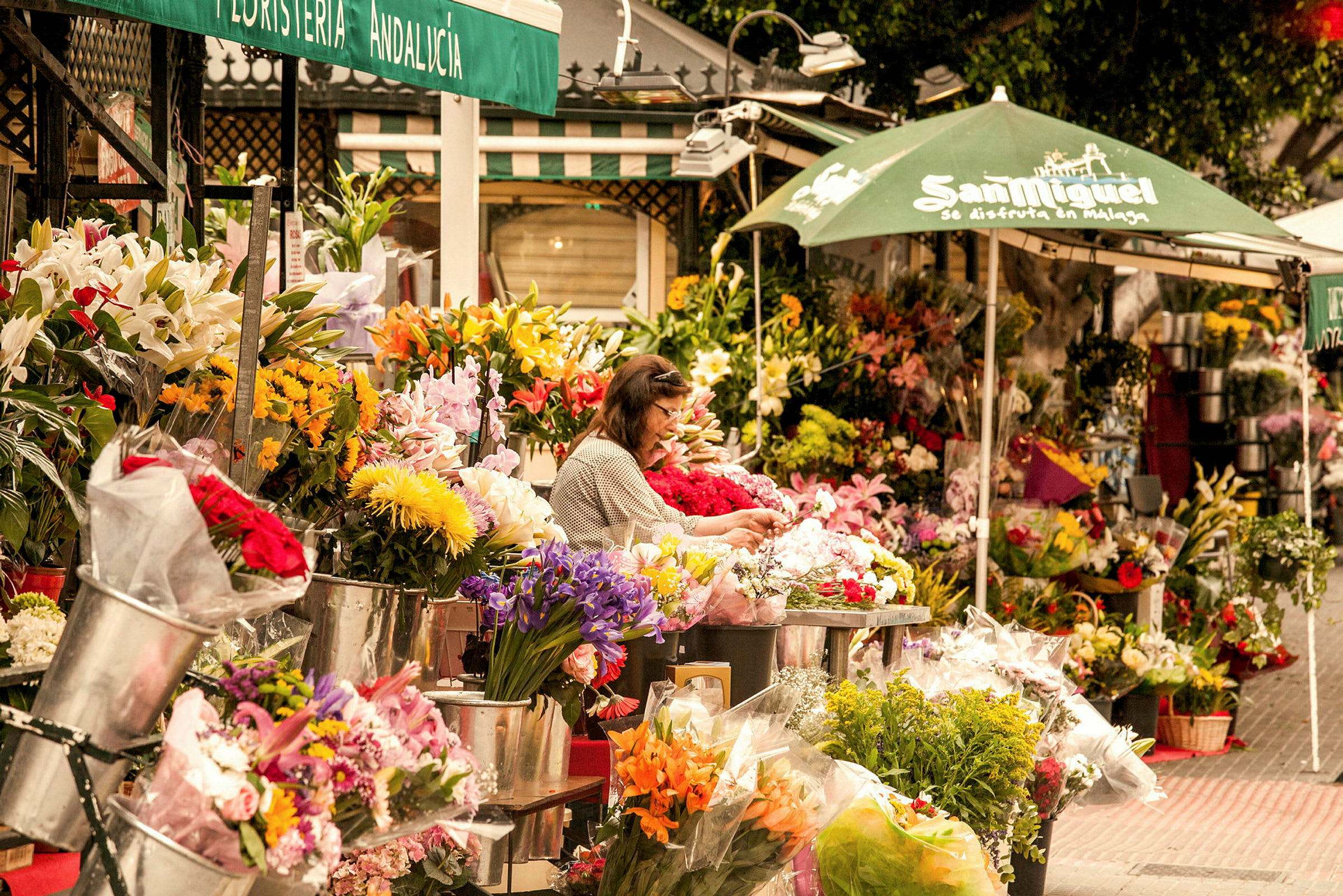 Blomsterstånd på en gata med olika färgglada buketter och arrangemang, samt en person som förbereder blommor. (AI-genererad text)