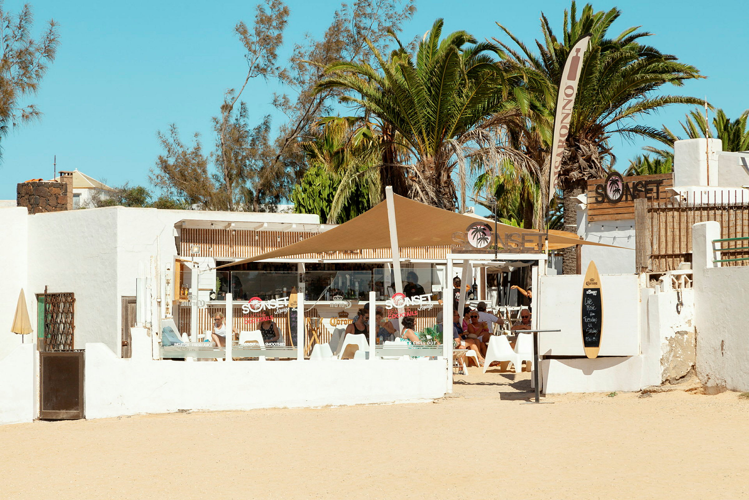 Ett strandkafé med vita väggar och palmträd i bakgrunden. (AI-genererad text)