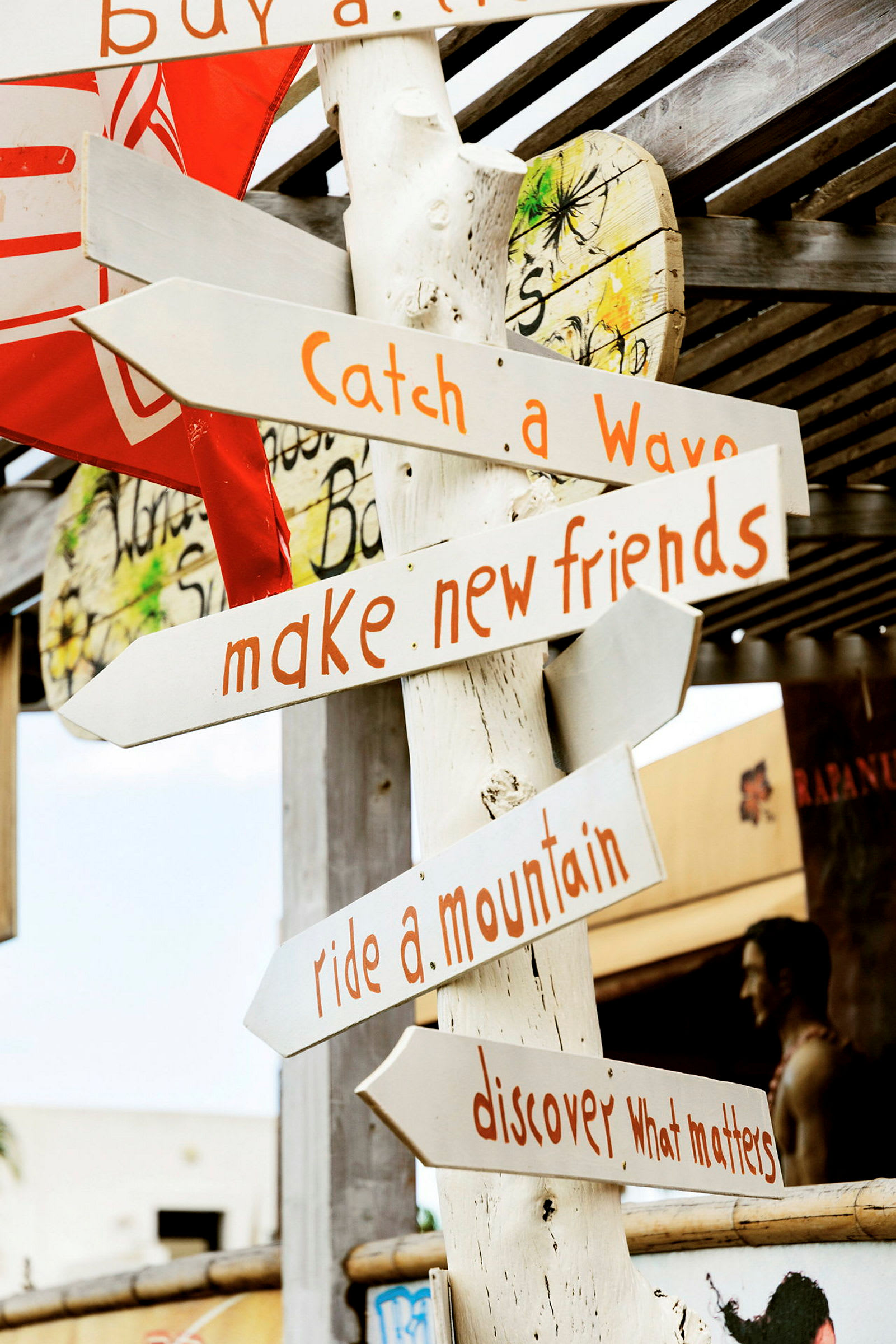 En träskylt med flera pilar i olika riktningar och texter som "Catch a Wave", "Make new friends", "Ride a mountain" och "Discover what matters". (AI-genererad text)