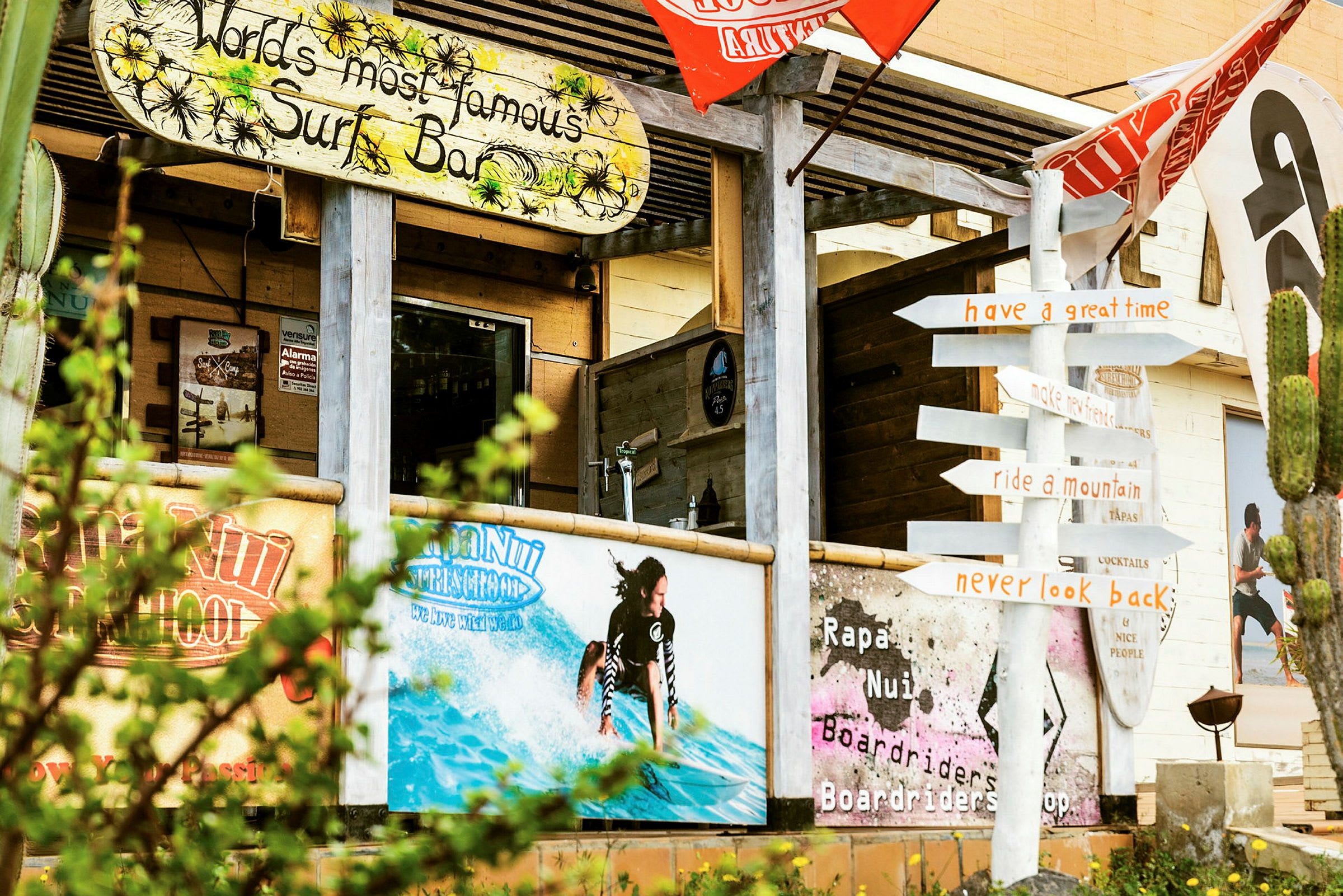 Ett surfhotell med färgglada skyltar och dekorationer, inklusive en figur av en surfare i vattnet, och en vägskylt som pekar i olika riktningar. (AI-genererad text)