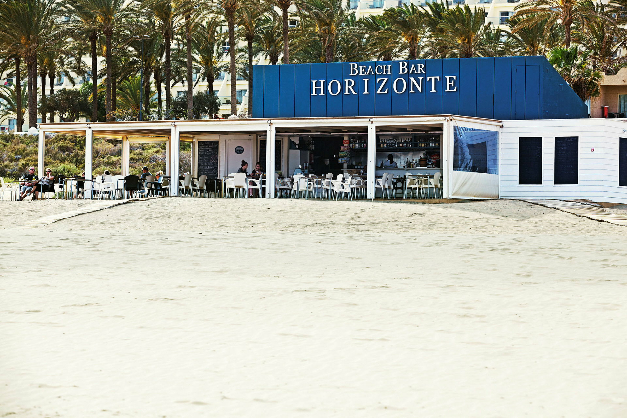 En strandbar med namnet Horizonte, belägen nära en sandstrand och omgiven av palmer. (AI-genererad text)