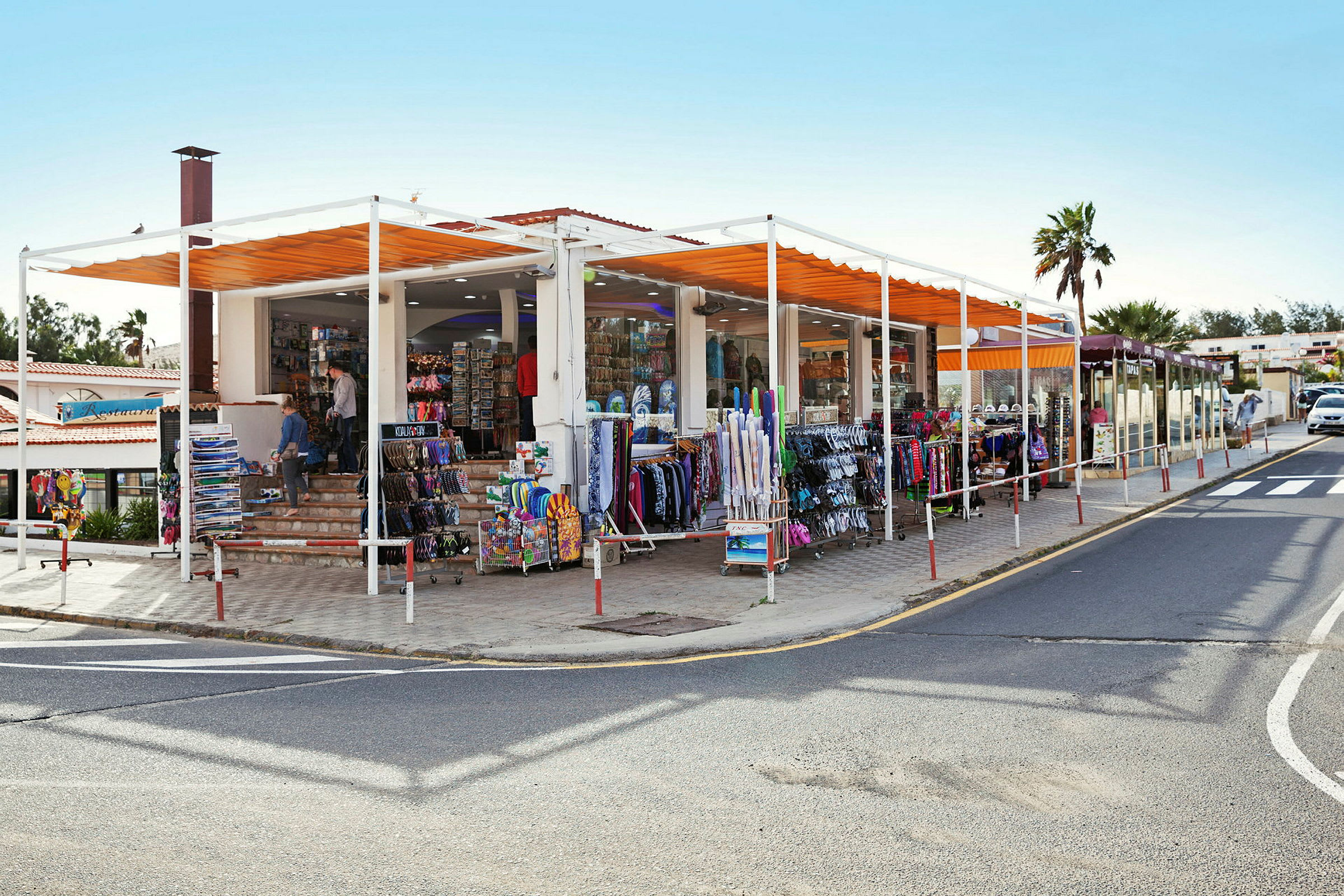 En butik med varor uppställda utanför, inklusive klädställningar och ställ med souvenirer, belägen vid sidan av en väg. (AI-genererad text)