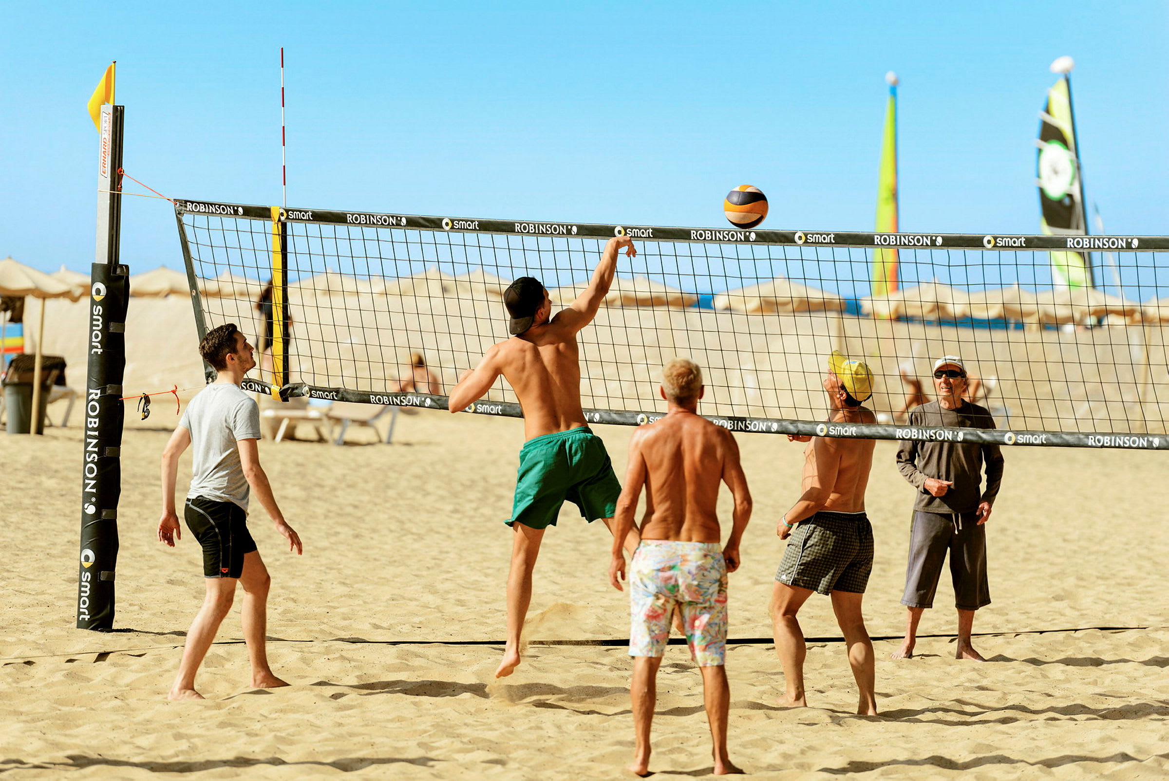 En grupp människor spelar beachvolleyboll på en sandstrand under en klarblå himmel. (AI-genererad text)