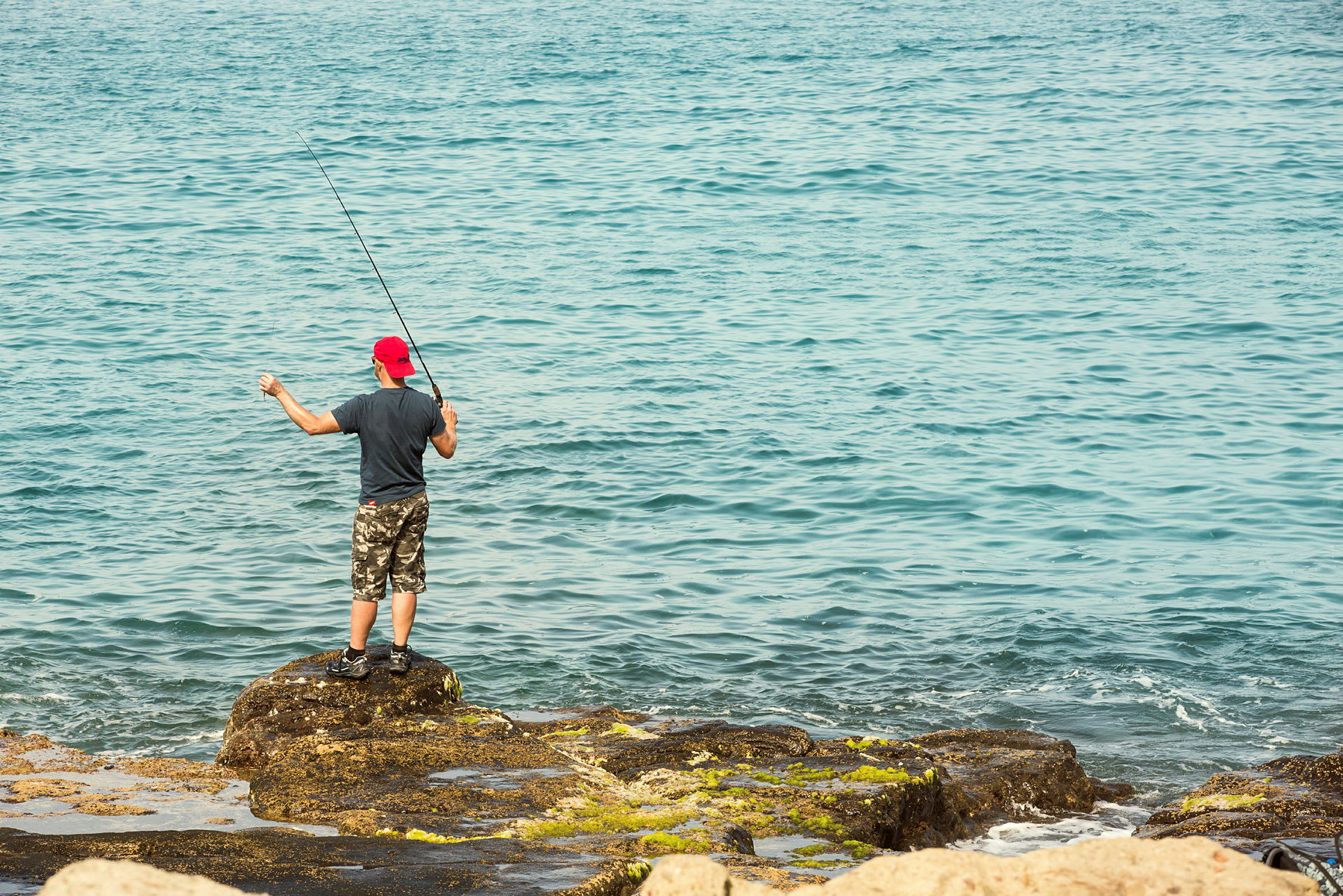 En person står och fiskar vid havet på klippor. (AI-genererad text)