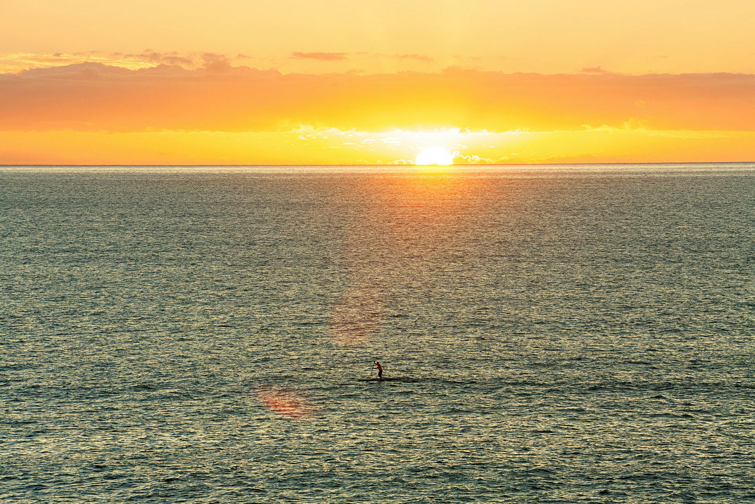 En solnedgång över havet med en person som står paddlande på en bräda. (AI-genererad text)