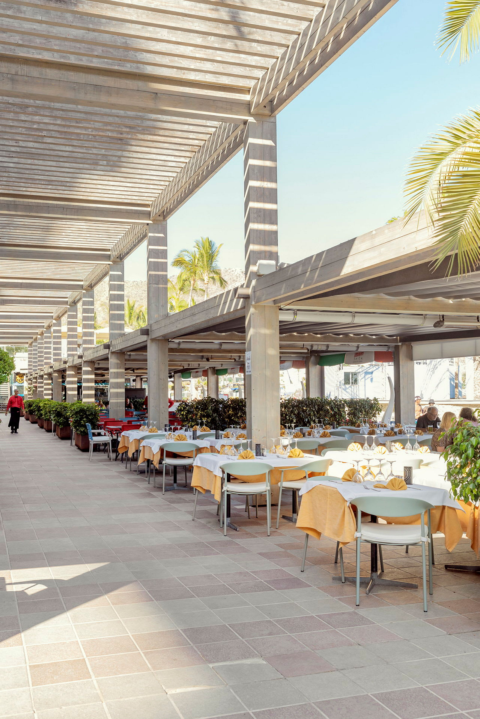 Uteservering med dukade bord och stolar under pergola. (AI-genererad text)