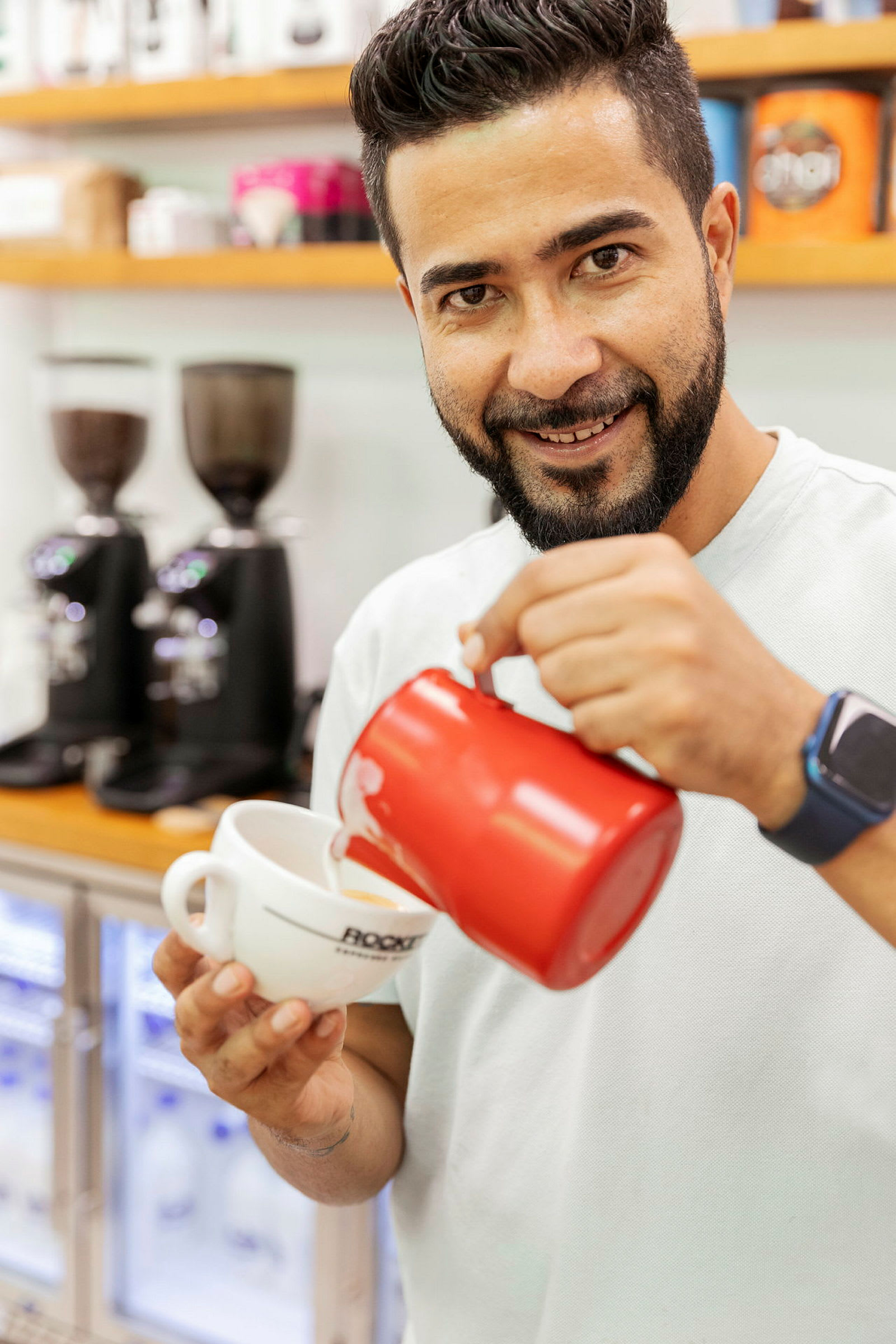 Person häller upp mjölk i en kaffekopp med en röd kanna. (AI-genererad text)