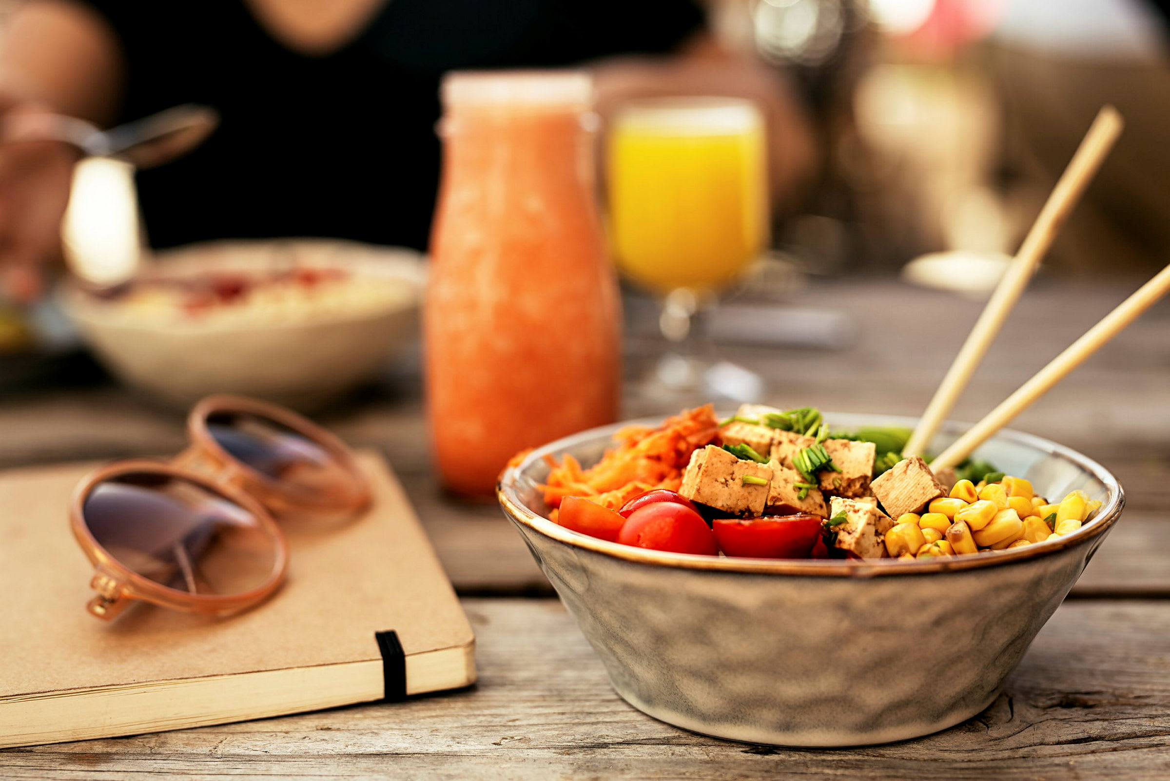 En skål med sallad, ett glas med orange dryck och ett glas med gul dryck på ett bord. (AI-genererad text)
