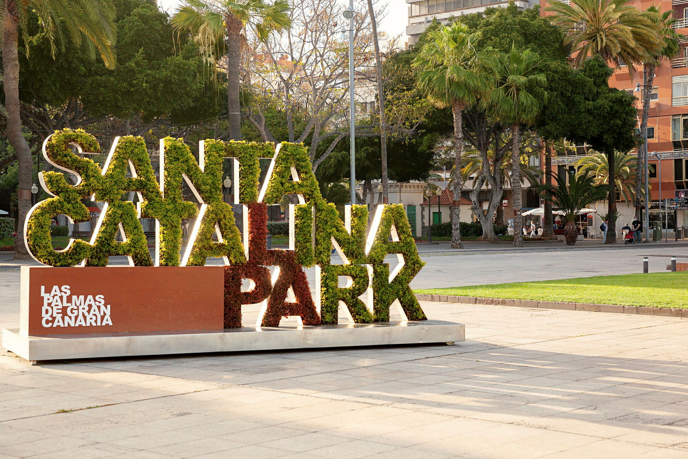 Skylt med texten 'Santa Catalina Park' fylld med grönska, omgiven av träd i stadspark. (AI-genererad text)