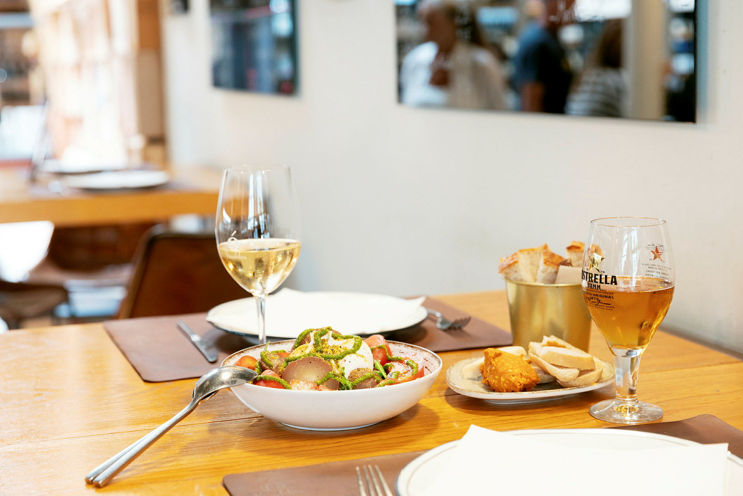 Ett bord med en salladsskål, glas vin, glas öl och en tallrik med bröd och tillbehör. (AI-genererad text)