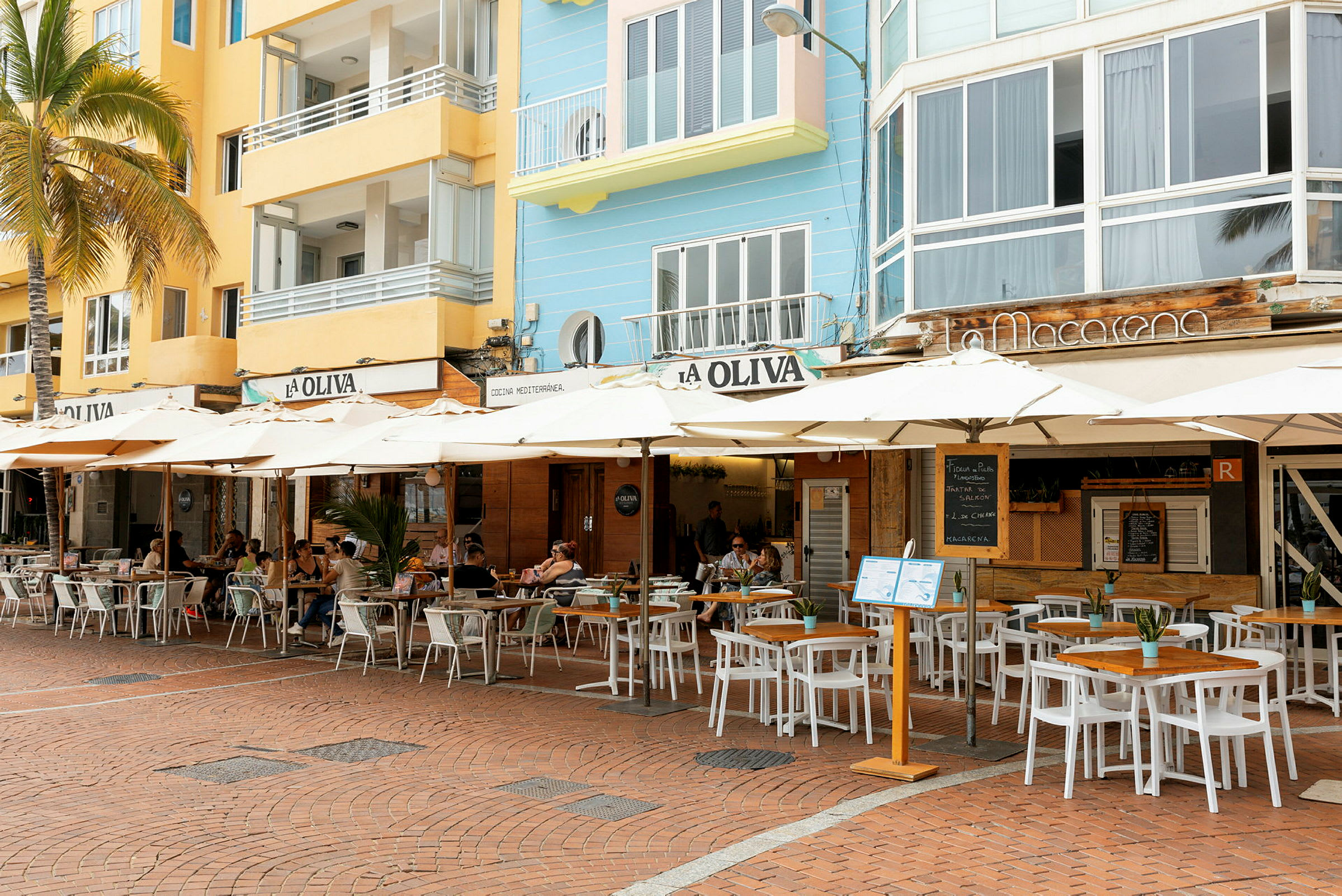 Utomhusservering vid en restaurang med färgglada byggnader i bakgrunden. (AI-genererad text)